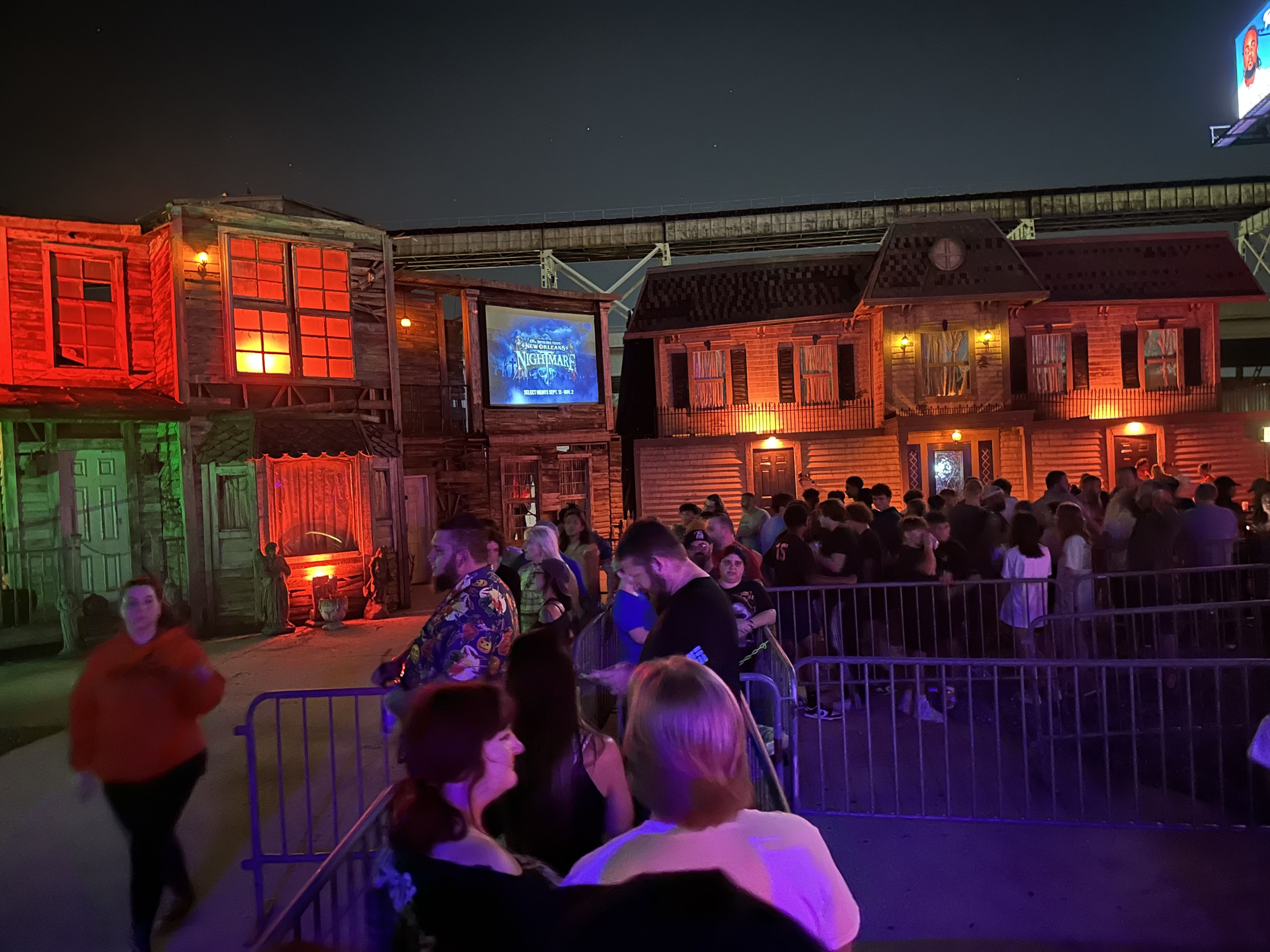 A line of people wait outside creepy buildings.