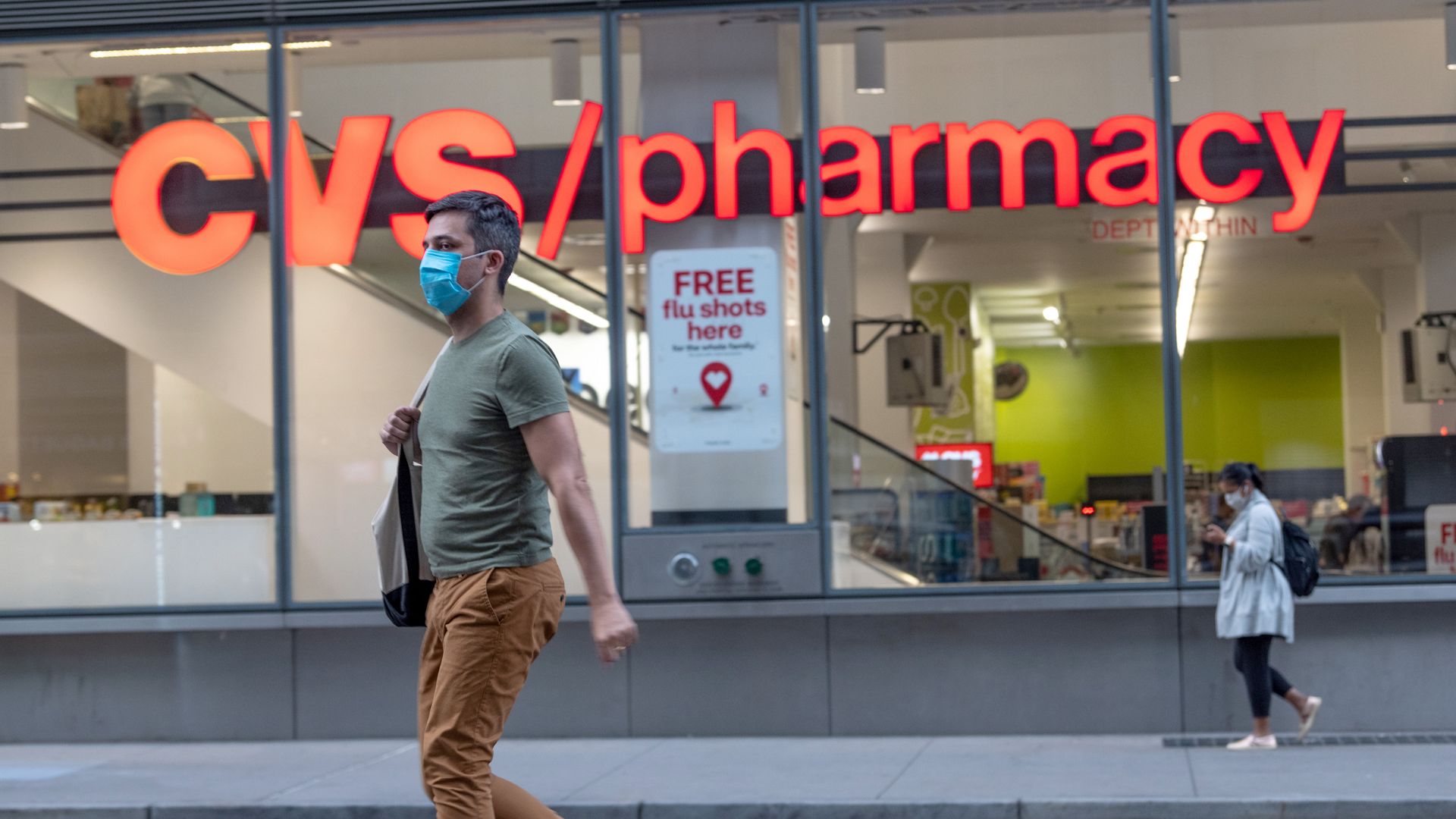 A man wearing masks walks past a CVS Pharmacy where a "Free flue shots here" sign