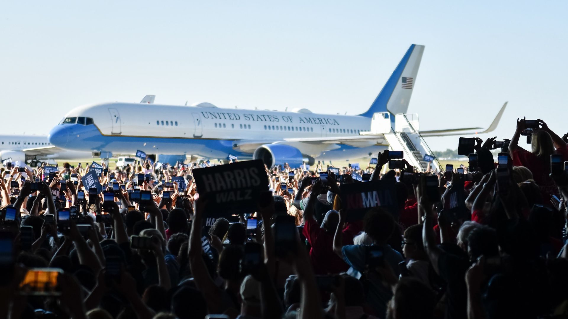 A large crowd cheering in front of a plane that has just landed.