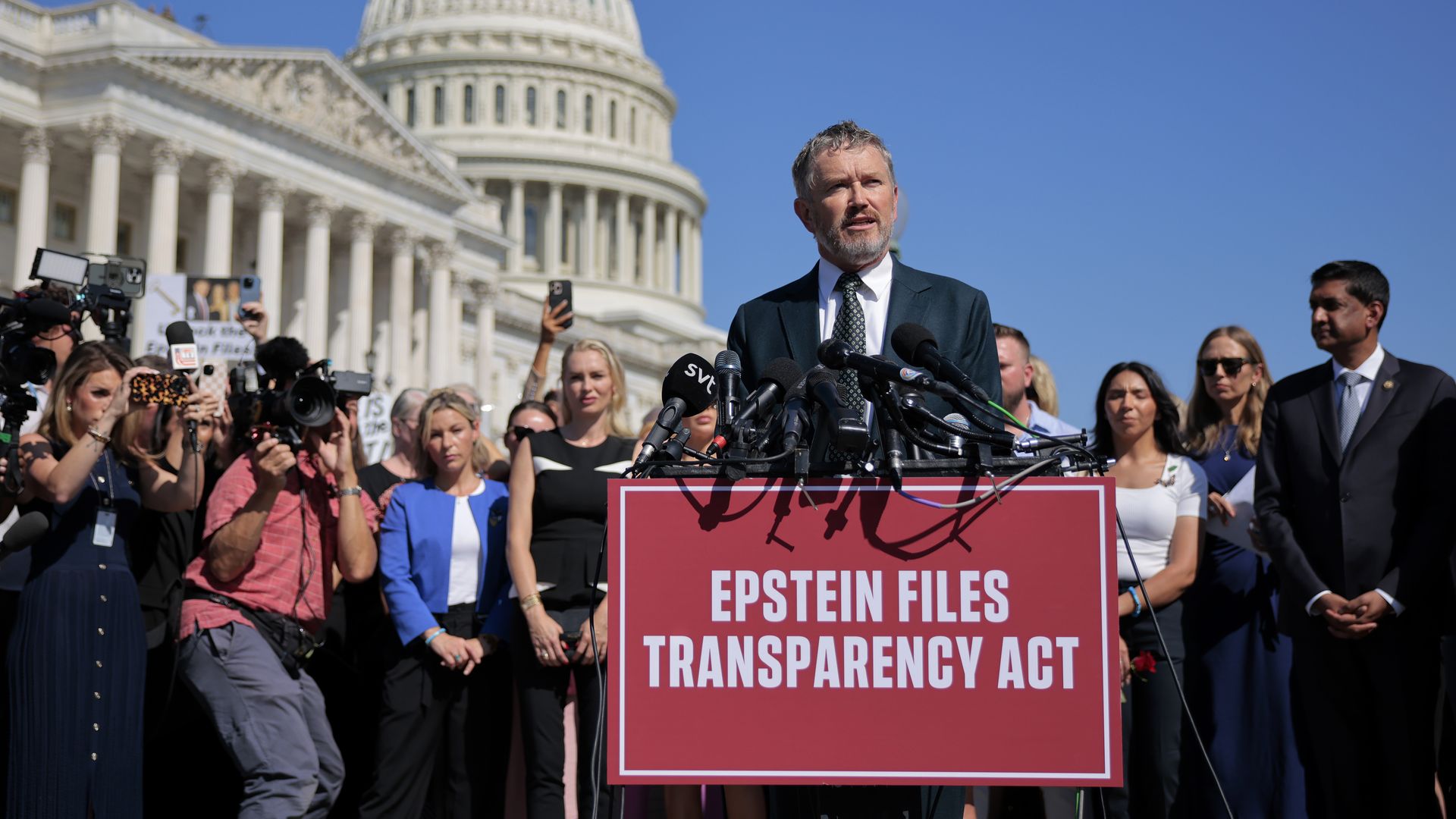 Congressman Massie wearing a blue suit speaks at a press conference with a crowd behind him, with the US Capitol Dome behind him. 