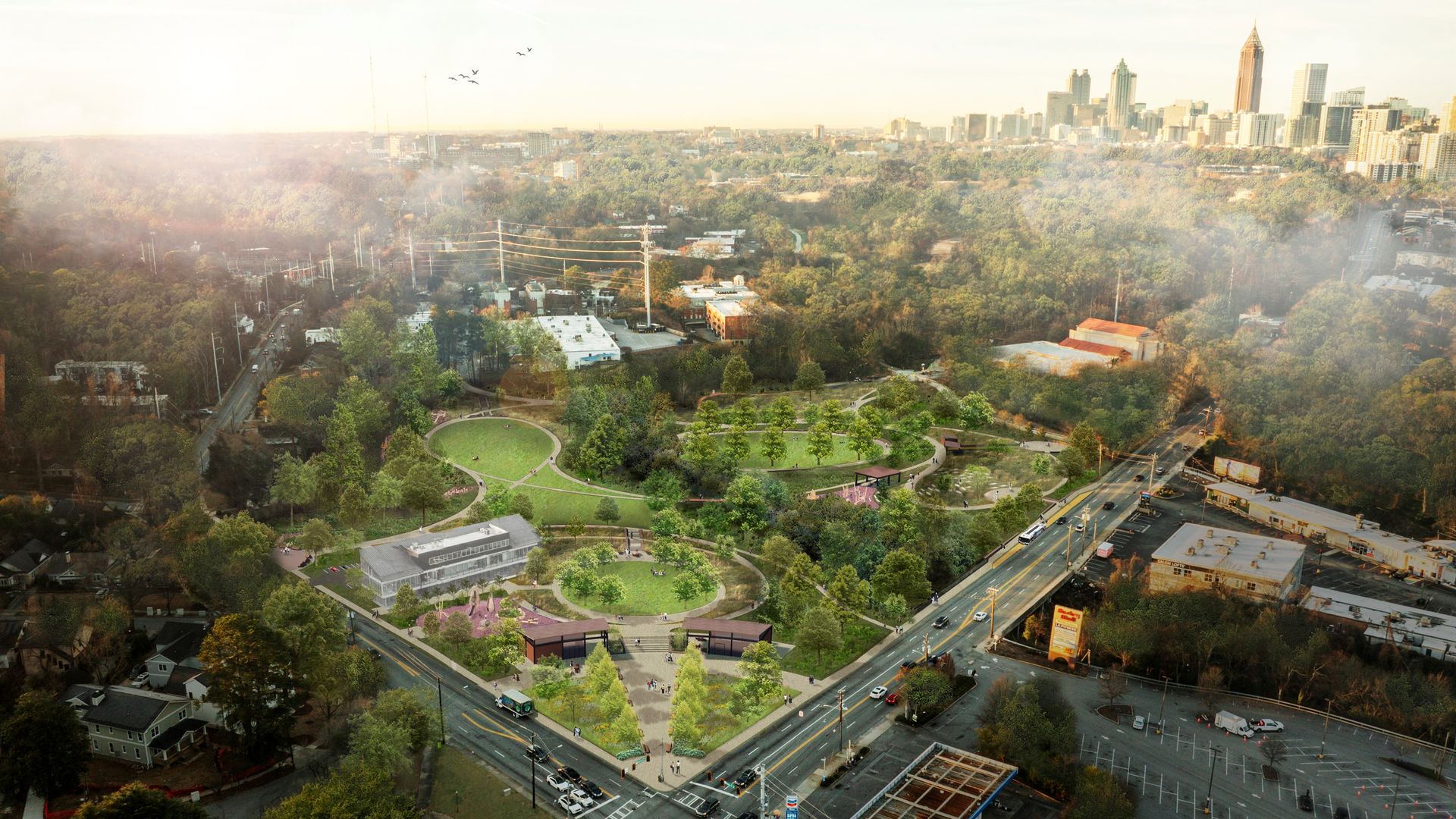 Panoramic city view with a dense forest park in the foreground, a circular green plaza, and a busy road. A distant skyline rises above trees under a hazy sky.