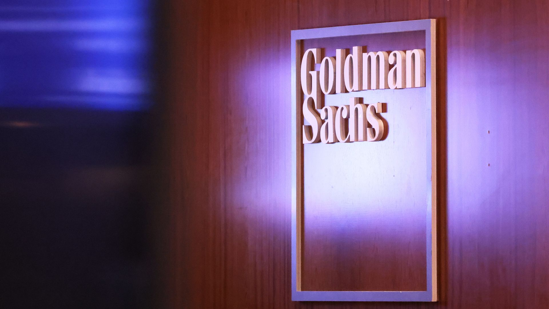 A Goldman Sachs logo hangs on a wood-paneled wall.