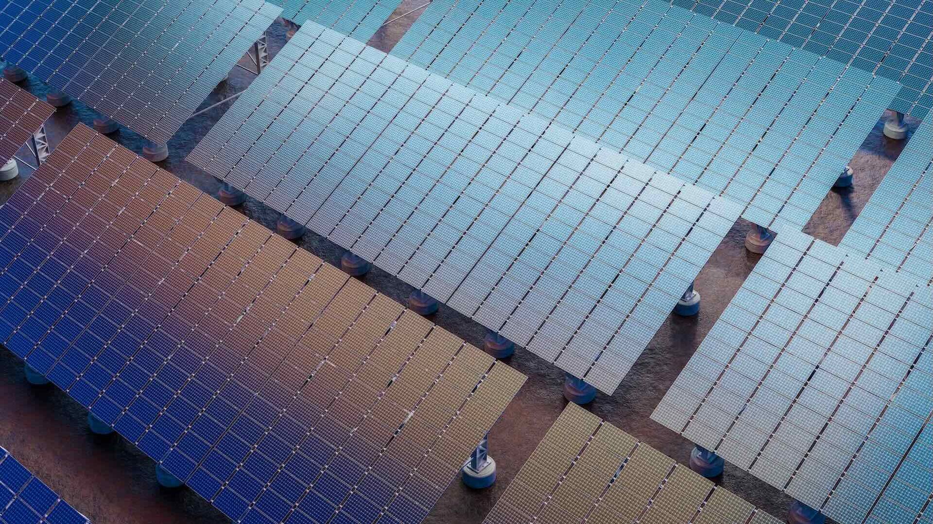 Overhead view of a solar farm with rows of blue and tan photovoltaic panels mounted on supports, creating a grid pattern across the ground.