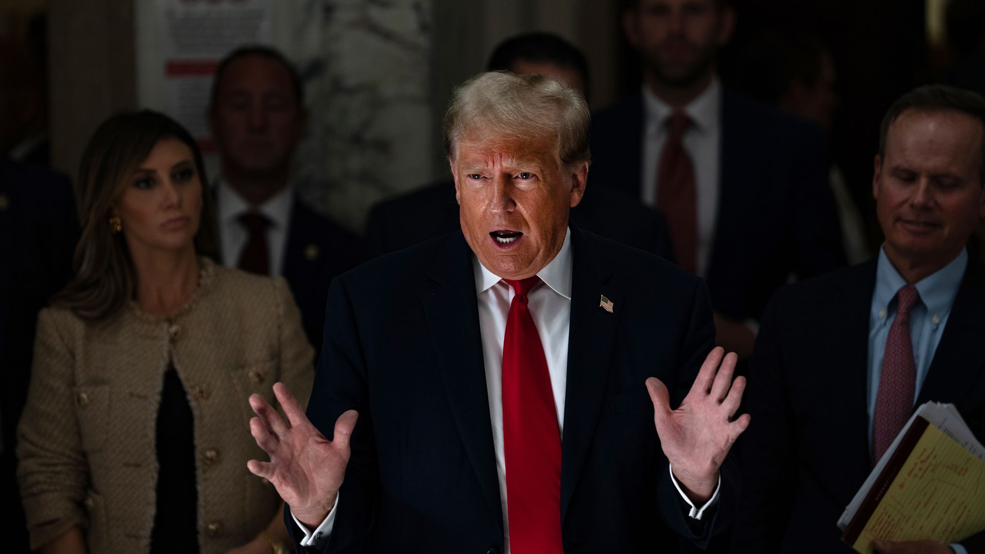 Trump speaks with hands outstretched wearing red tie.
