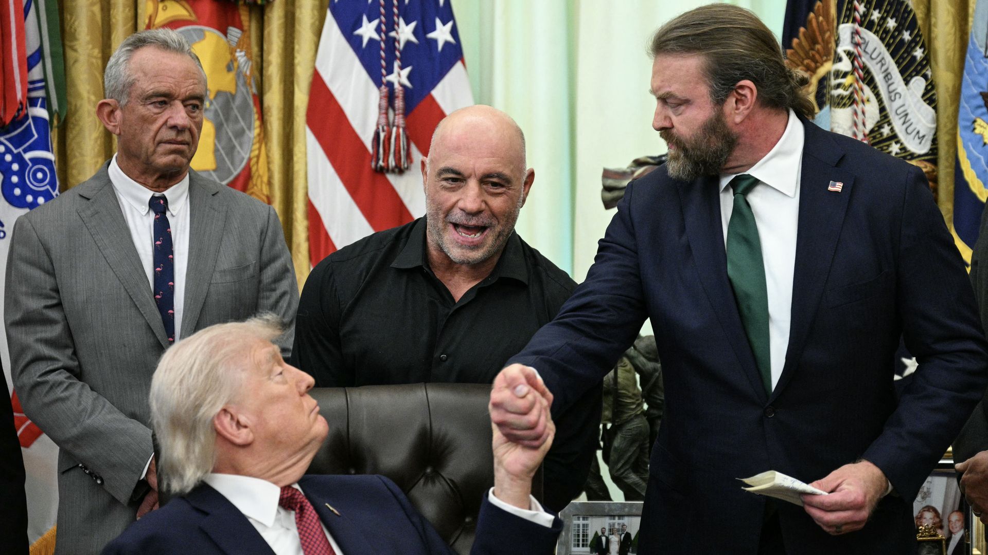 (L/R) US Secretary of Health and Human Services Robert F. Kennedy Jr., and US media personality Joe Rogan look on as US President Donald Trump shakes hands with W. Bryan Hubbard, CEO of Americans for Ibogaine, during an executive order signing ceremony in the Oval Office of the White House in Washin