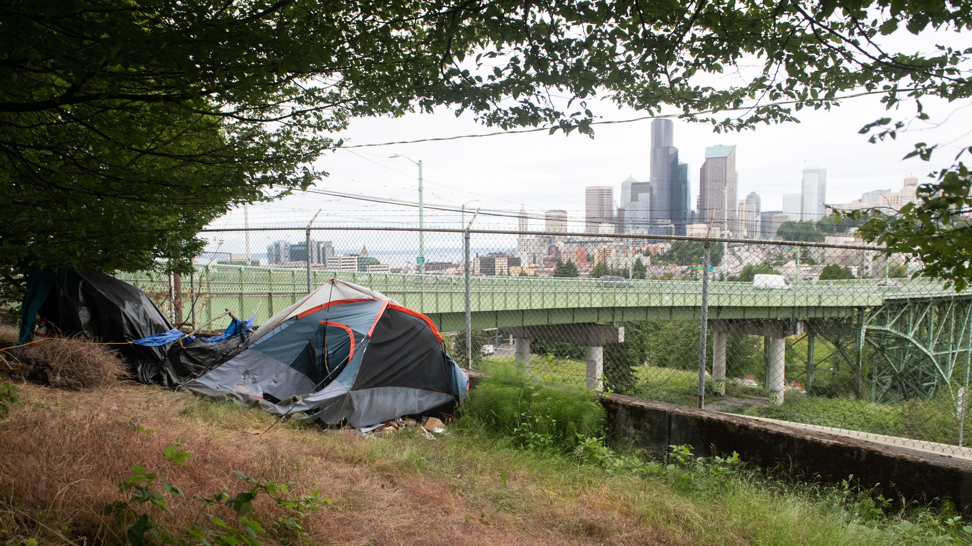 A tent is set up near roads and a chain link fence with Seattle in the background. 