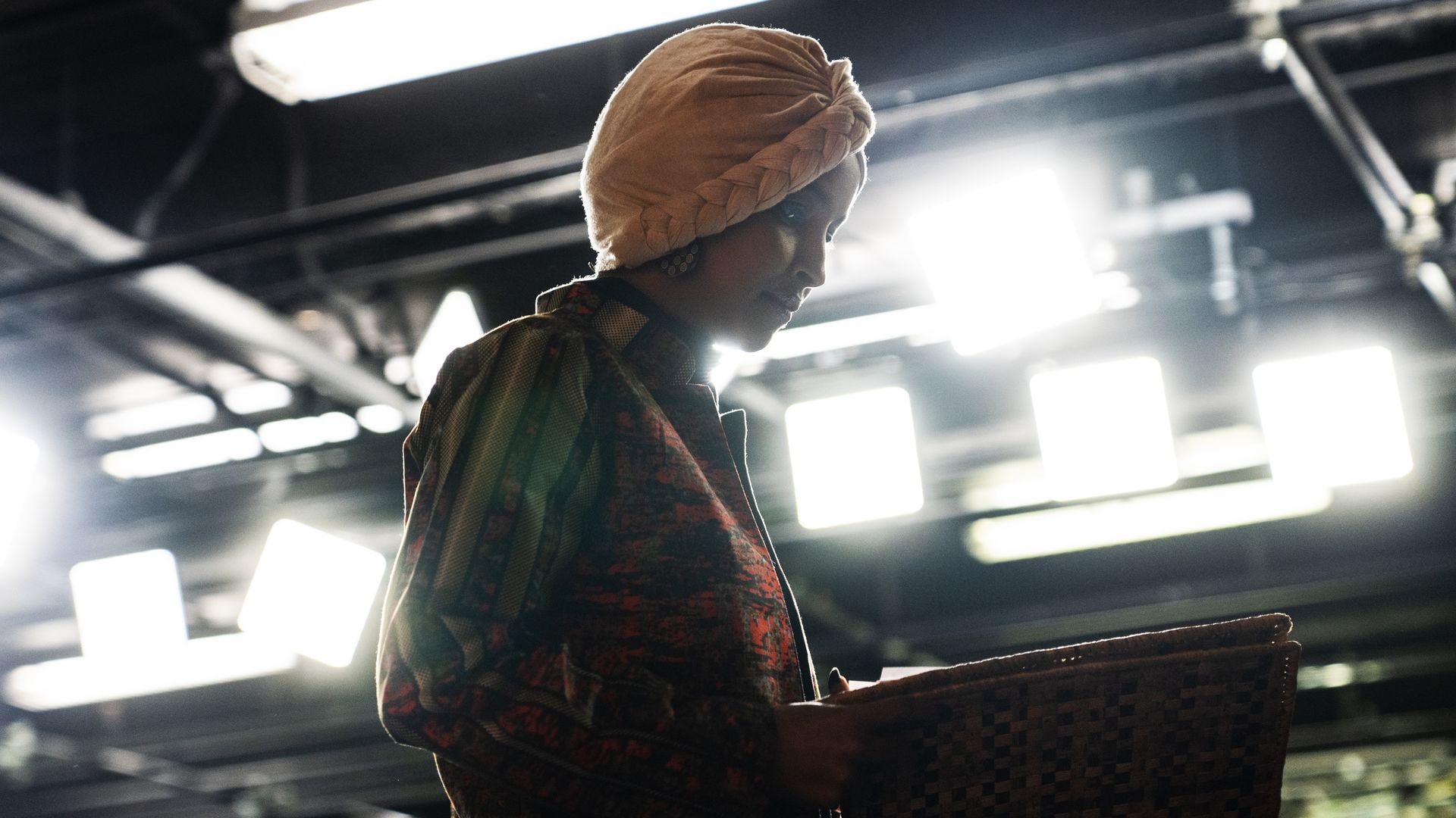 Rep. Ilhan Omar, wearing a peach-colored headscarf, looks at a binder while standing under studio lights.
