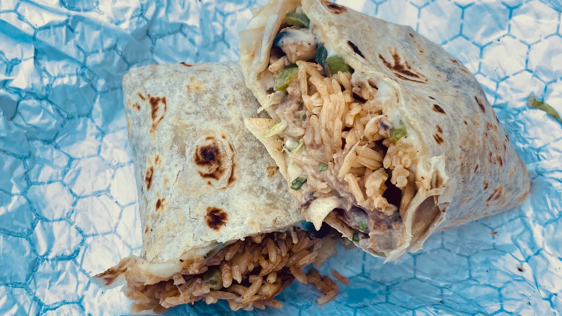 Two halves of a burritos rest on a paper food wrapper.