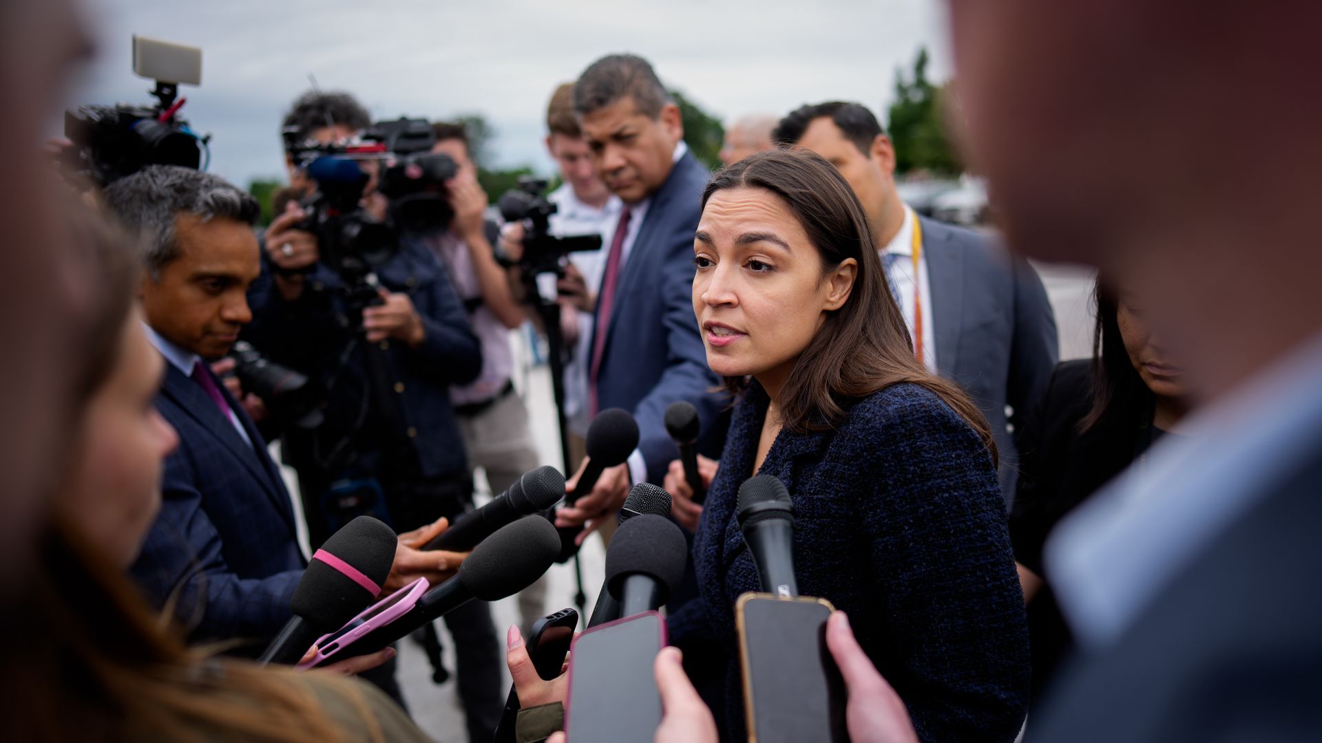 Alexandria Ocasio-Cortez speaks to reporters carrying several microphones