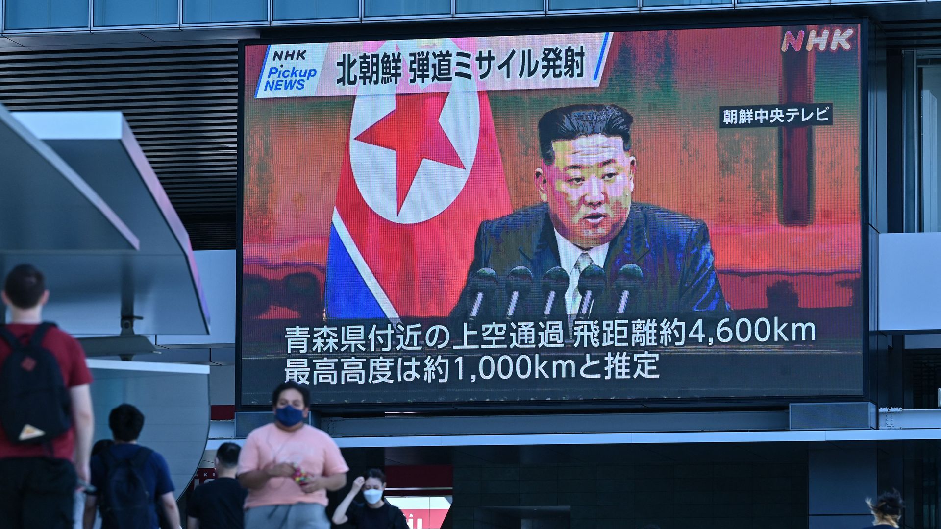 Pedestrians walk under a large video screen showing images of North Korea's leader Kim Jong Un during a news update in Tokyo on October 4, 2022