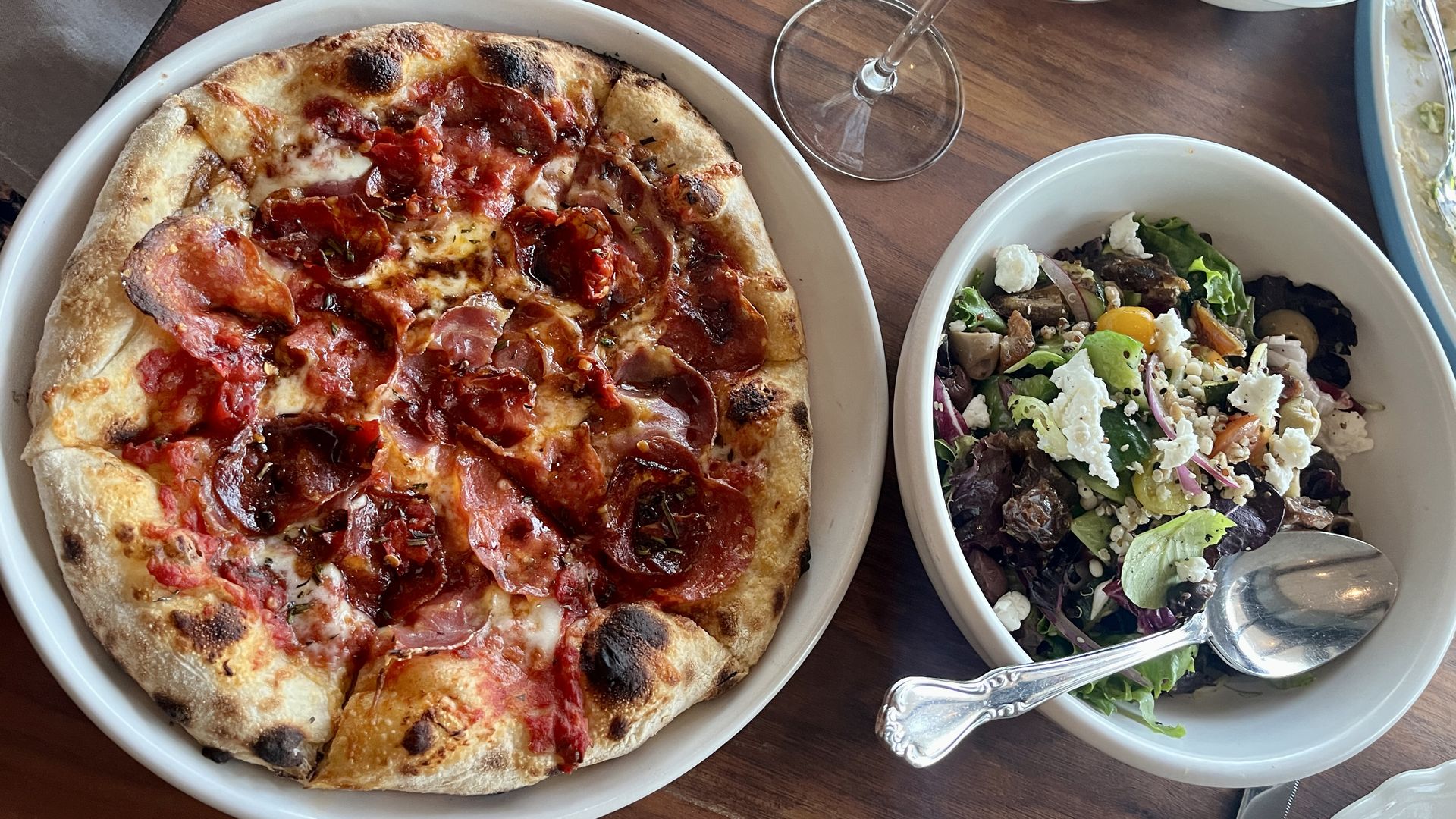 A salad, pizza and wine glass. 