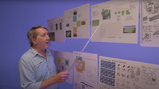 Photo of game designer Will Wright holding a pointer and looking at diagrams related to his new game