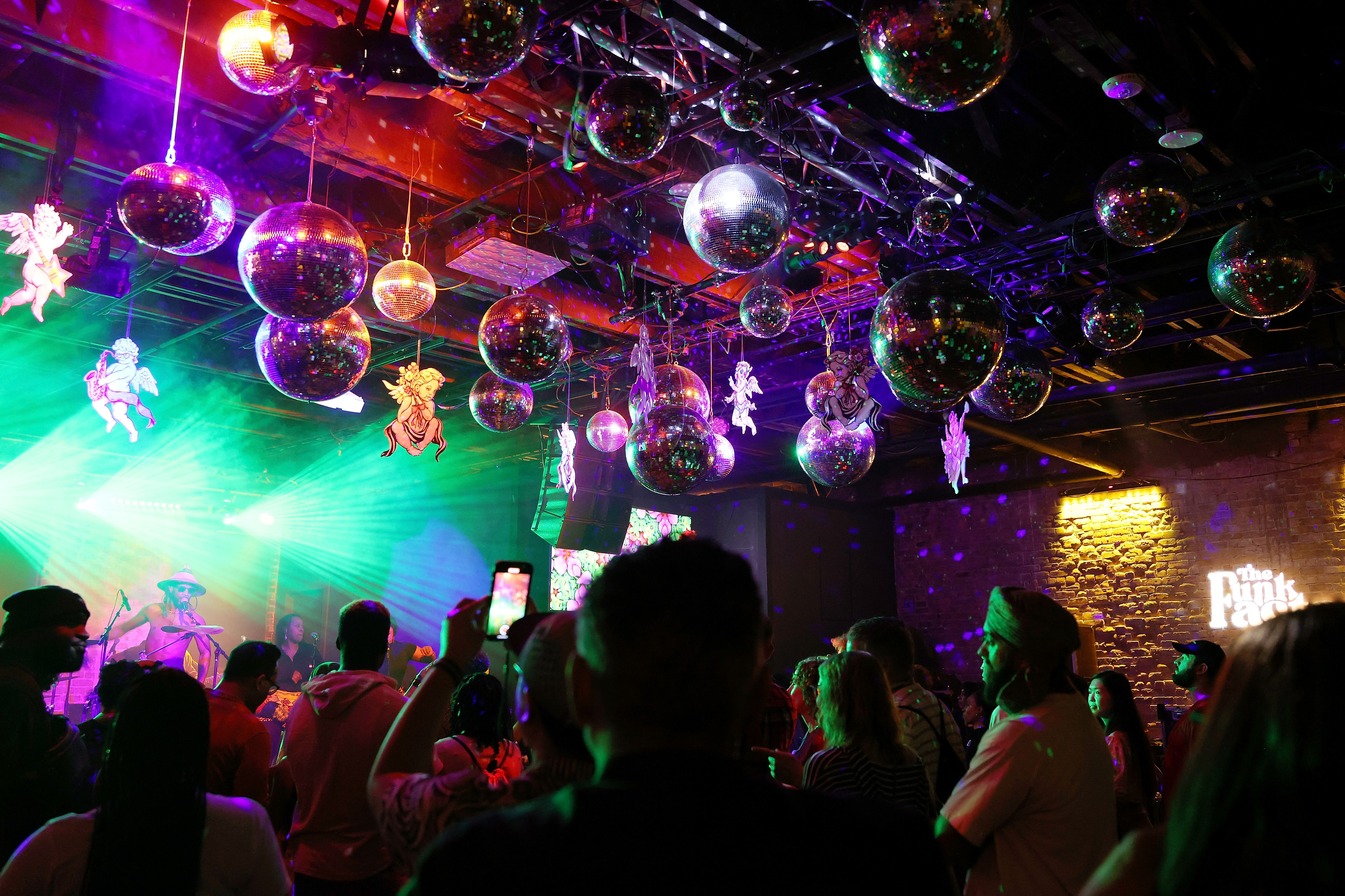 Disco balls hang from the ceiling while a crowd listens to music underneath.
