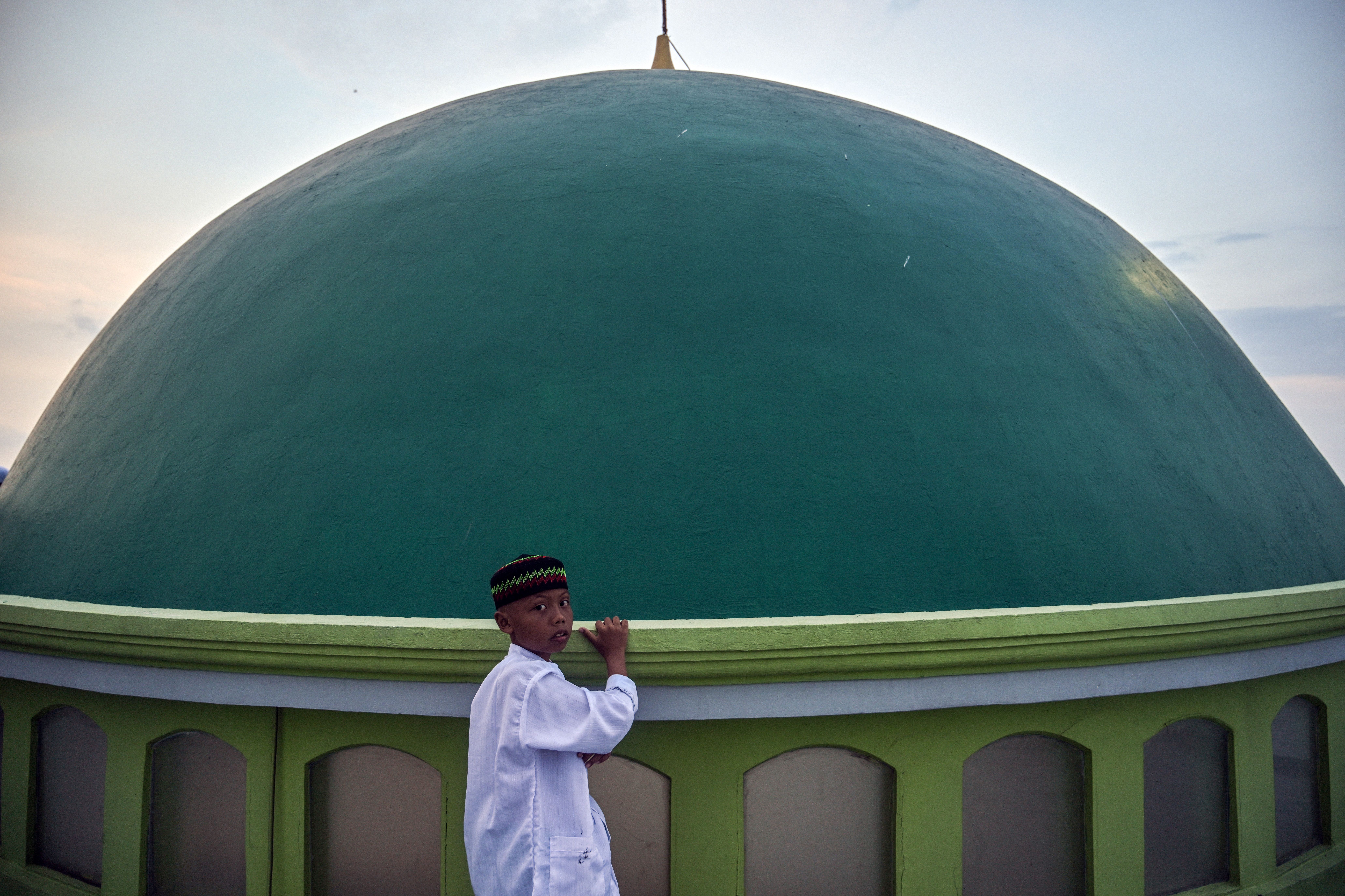 Child in white holds edge of green mosque dome