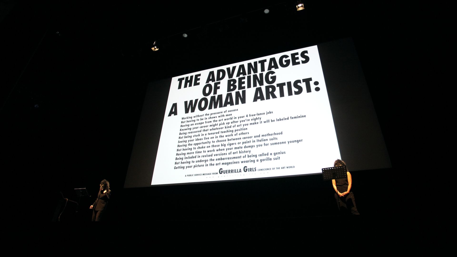 Projected on a screen, a presentation reads: "The advantages of being a woman artist:"