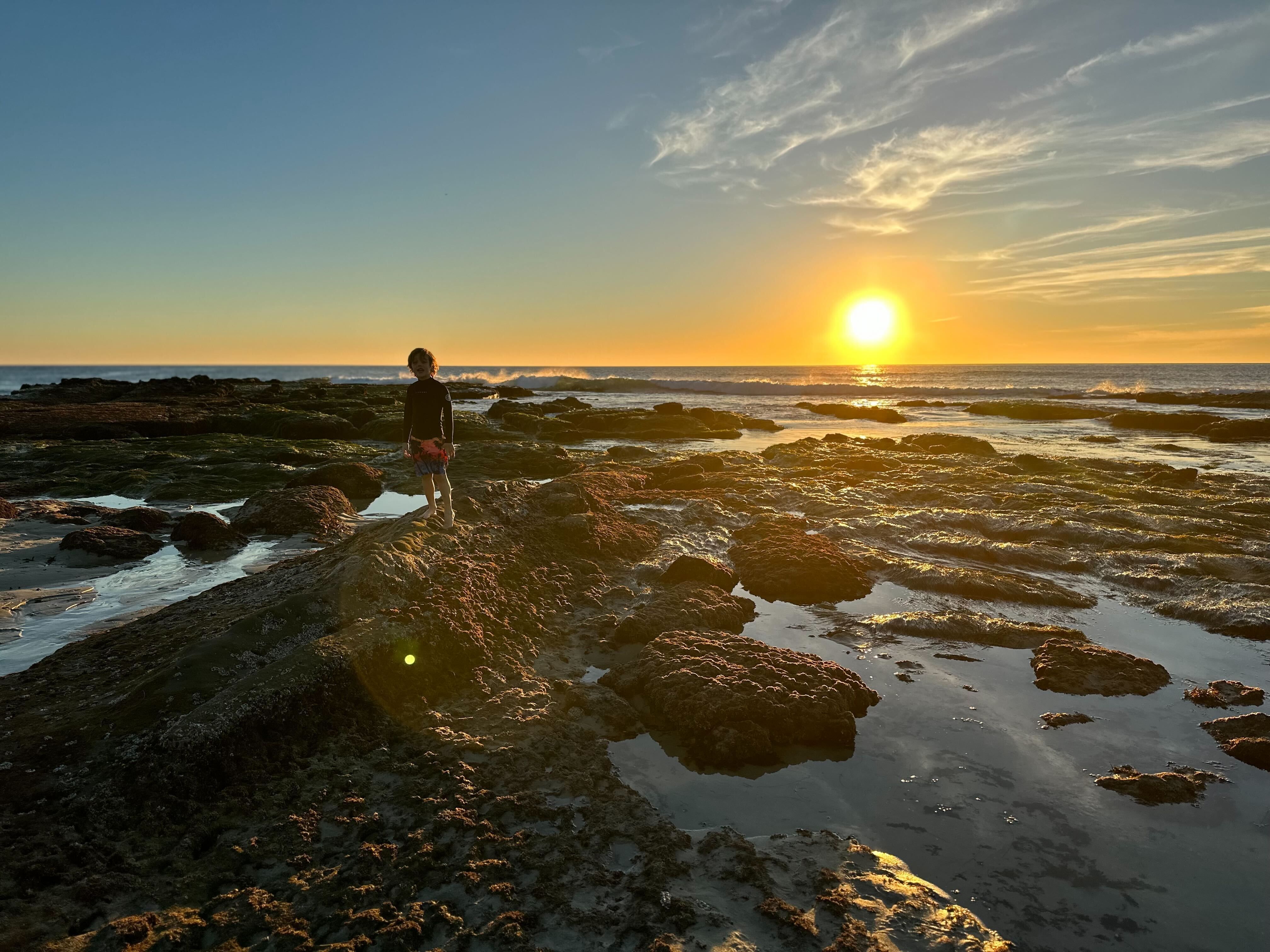 A young boy explores tide pools at Windansea beach at sunset