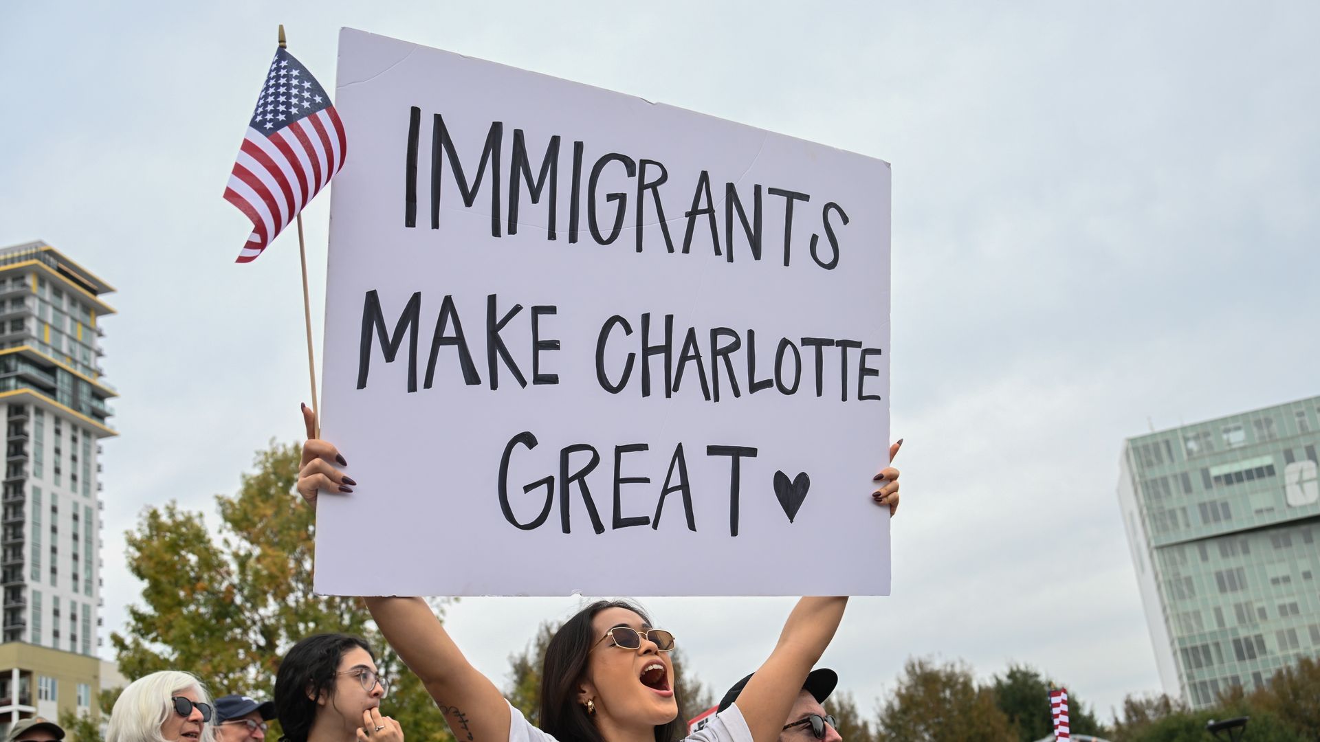 A woman yells as she holds an American flag and a sign in the air that reads, "IMMIGRANTS MAKE CHARLOTTE GREAT."
