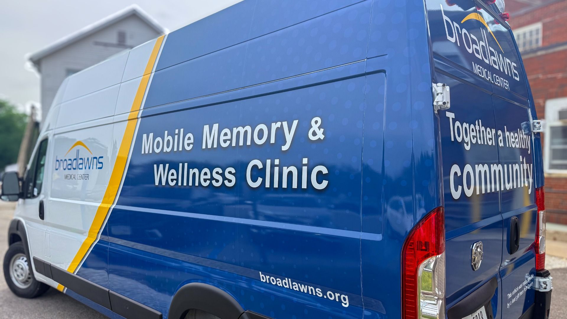 Blue Broadlawns medical van featuring large white text 'Mobile Memory & Wellness Clinic' and 'Together a healthy community,' with a yellow diagonal stripe along the side.