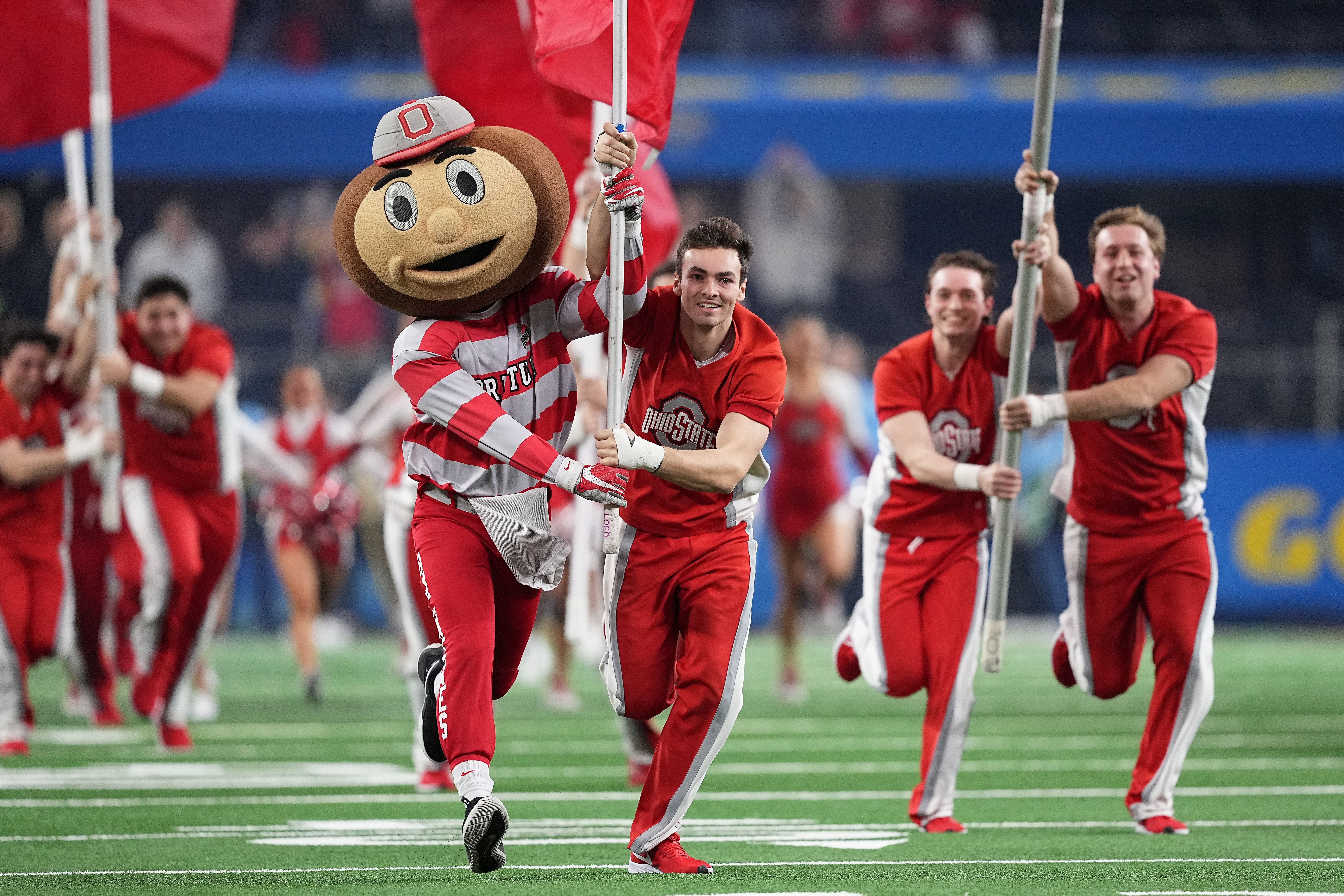 Ohio State's mascot and cheerleaders run across the field at the start of a football game carrying the school's flags.