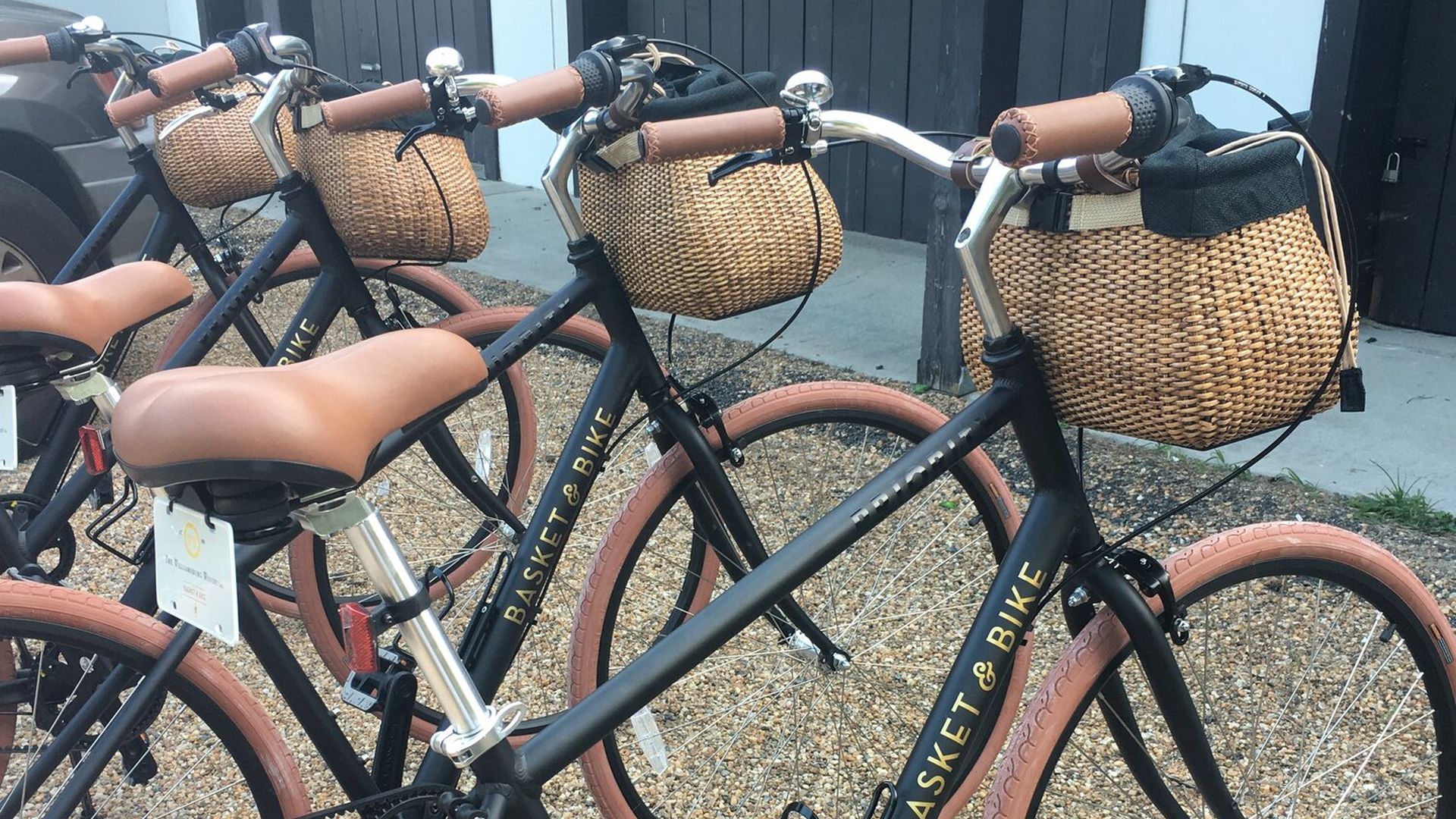 Image shows bicycles lined up on a sidewalk - and all have baskets on the front of the bikes. 