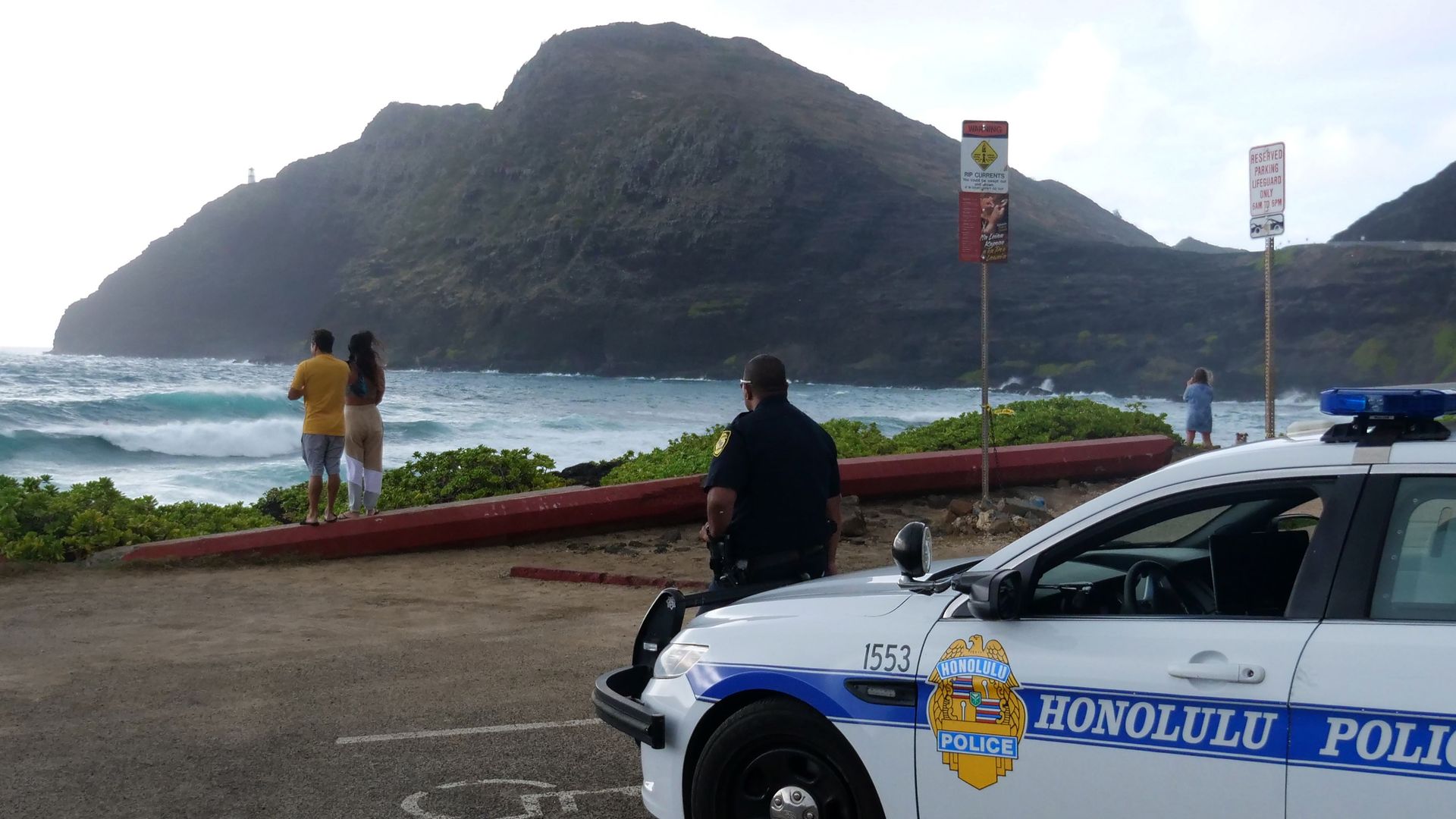 Police wait for people to return to their cars before closing the beach parking lot in preparation for Hurricane Douglas, in Honolulu, Hawaii, on Sunday.