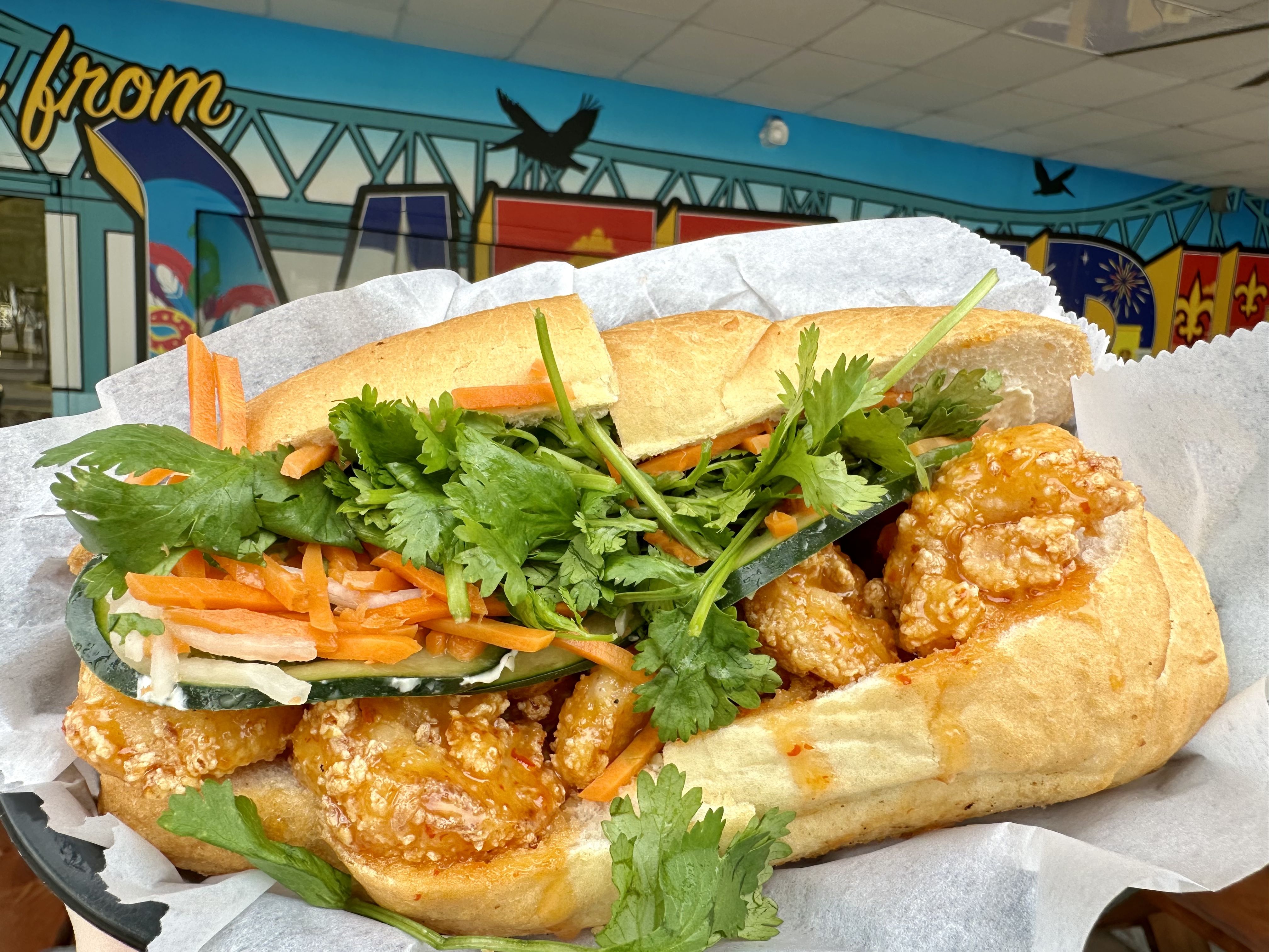 Photo shows a banh mi stuffed with fried shrimp and crunchy veggies