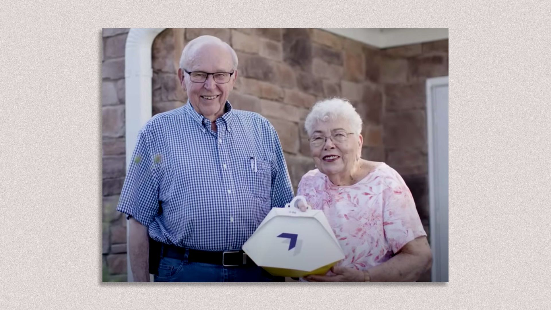 Photo of Susie (84) and Paul (83) Sensmeier, holding a small box delivered by Wing's drone delivery service. 