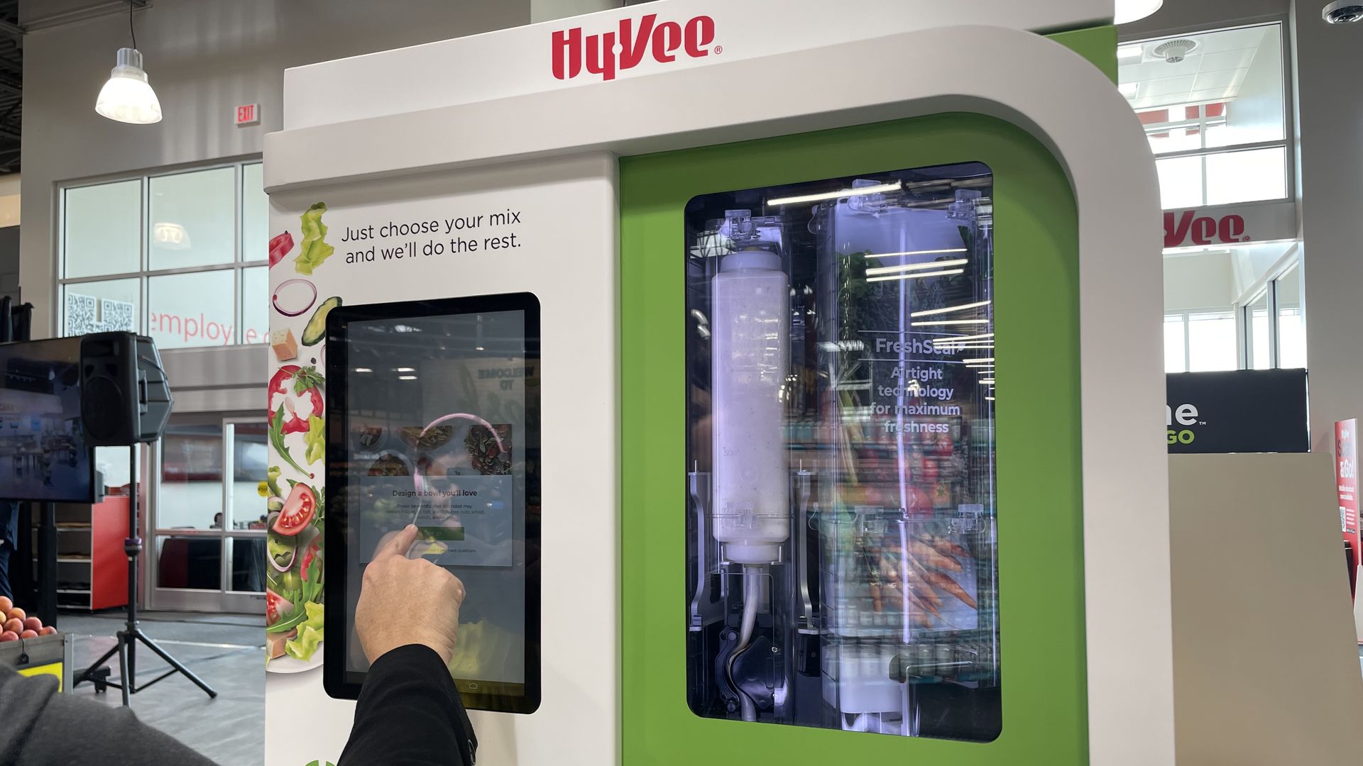 A green and write kiosk, where a person orders a salad that is made inside 