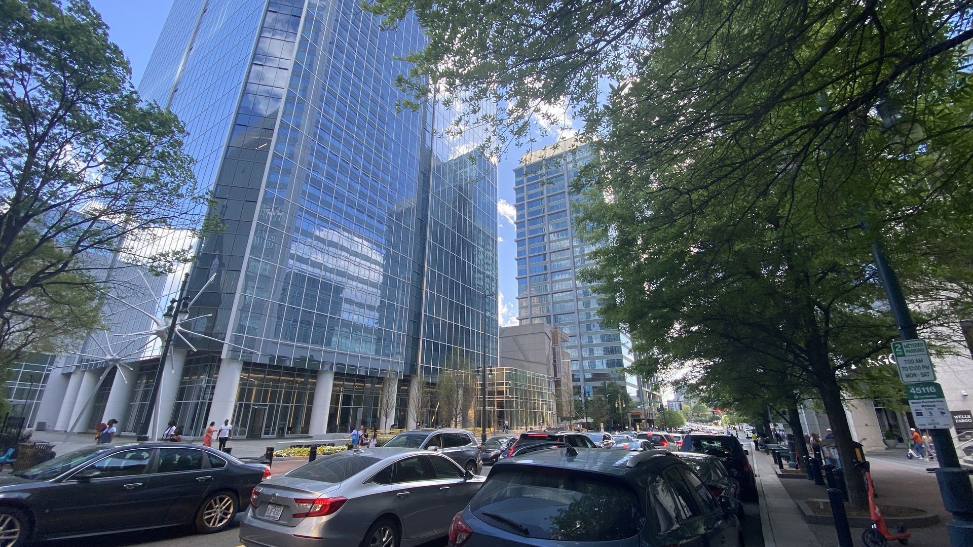 Skyscrapers to the left, people walking on the sidewalk, cars fill the street and green trees line the right side of South Tryon Street in Uptown. 