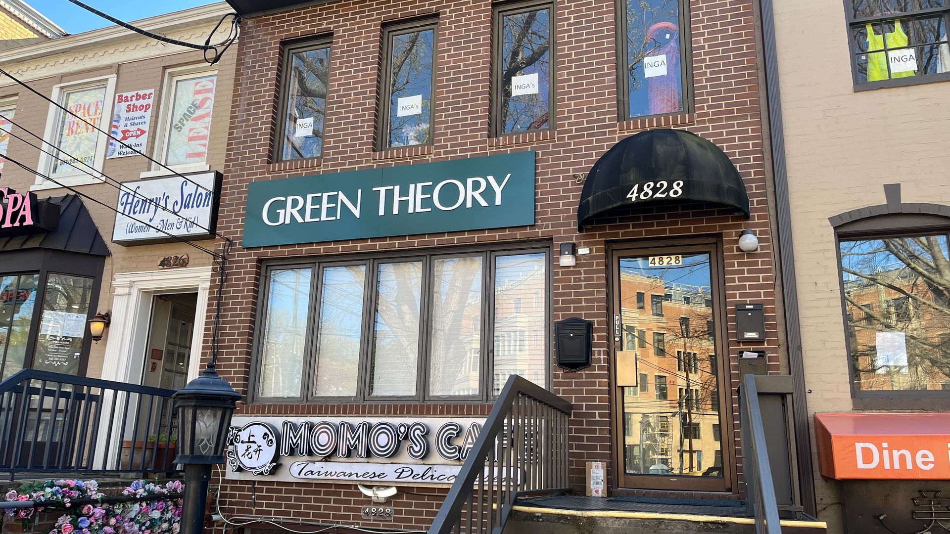 The storefront (with sign "Green Theory") sandwiched between a carryout, barber and other businesses.