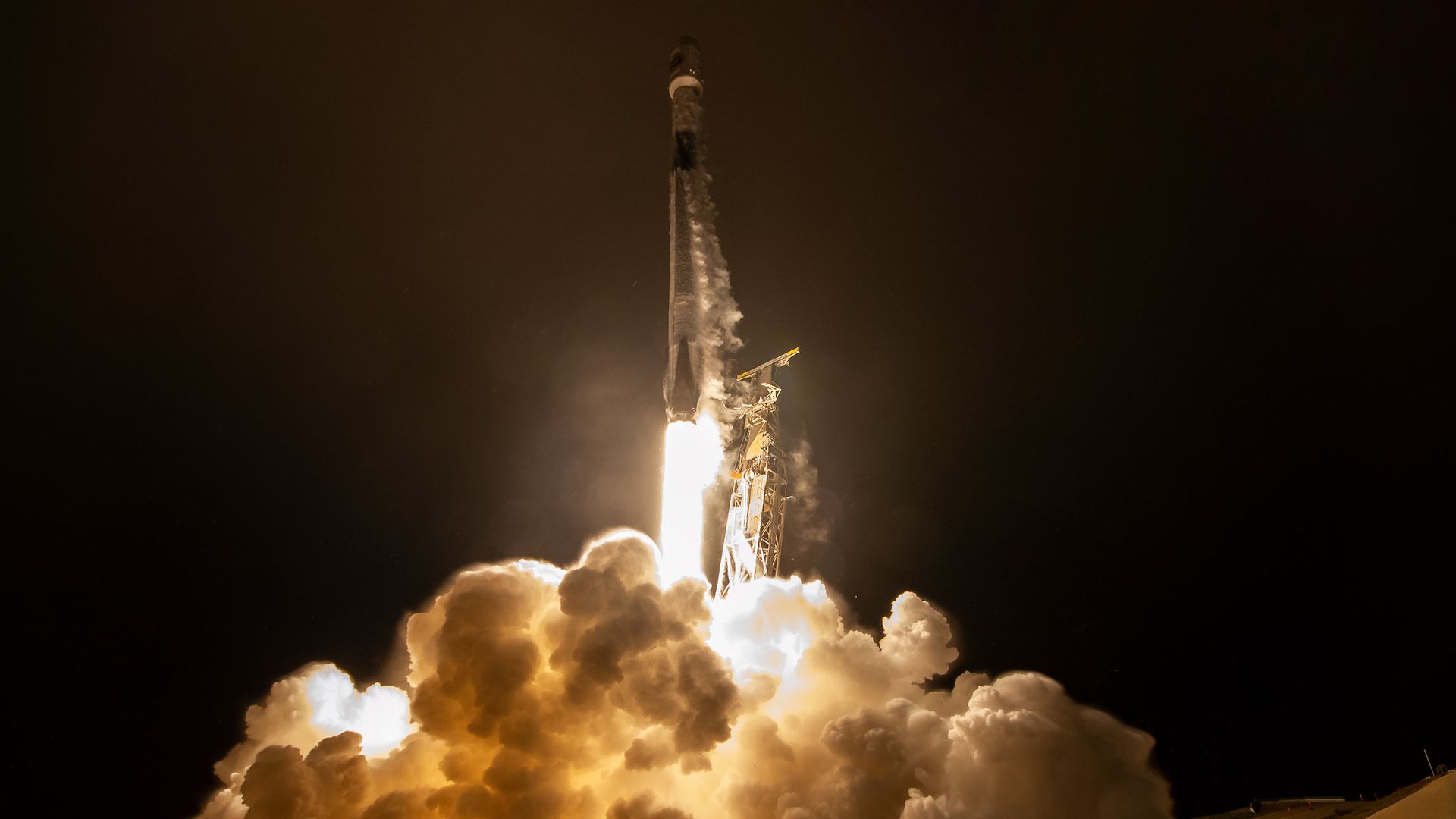 A plume of vapor blasts into the air around a Falcon 9 rocket rising into a dark sky