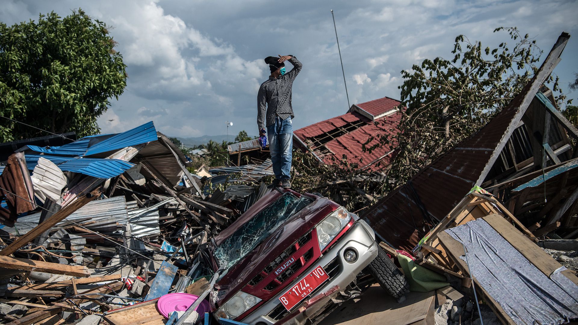 A man stands on a destroyed car as he views the rubble and debris of destroyed buildings following an earthquake in Palu, Indonesia. 