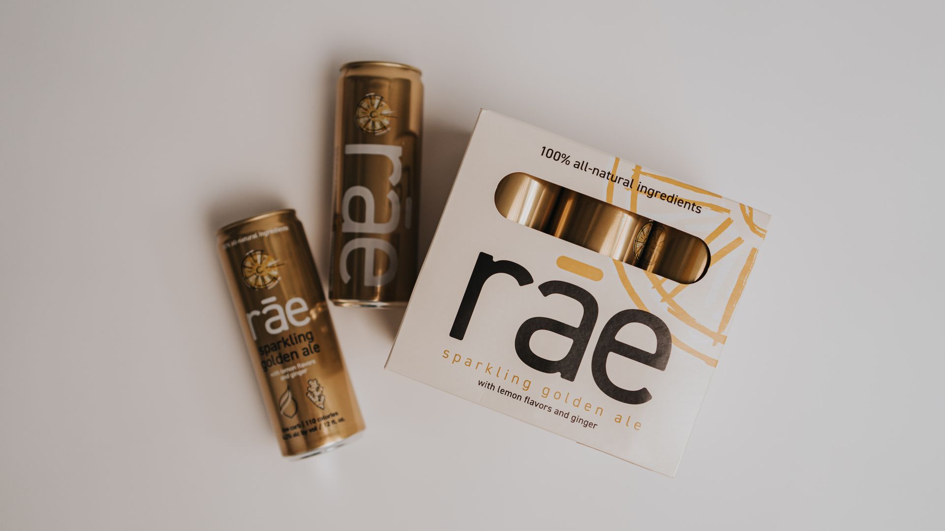 A white box of cans with rae written on it and two gold cans next to it. 