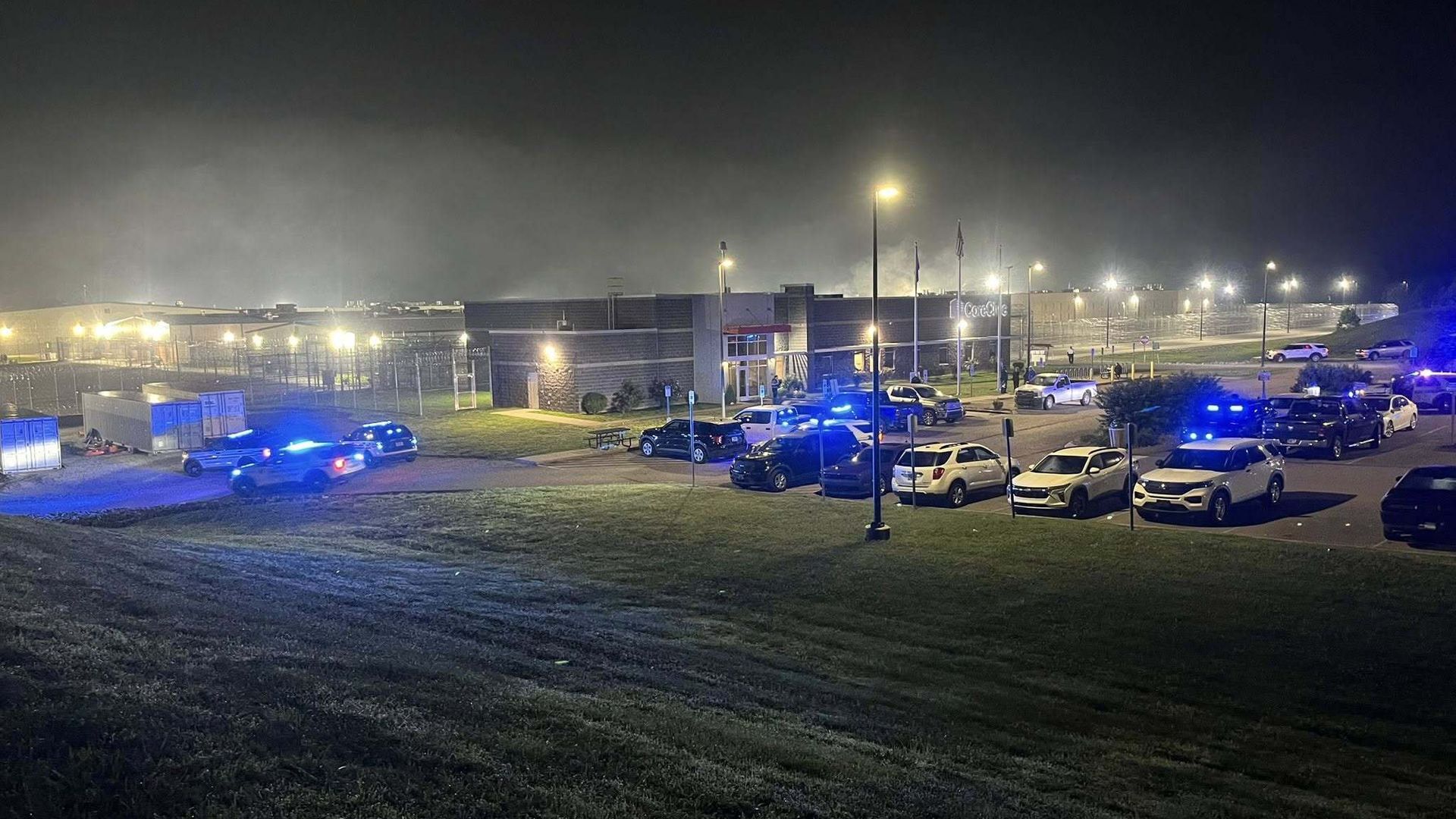 Law enforcement vehicles with blue lights flashing in the parking lot of a building.