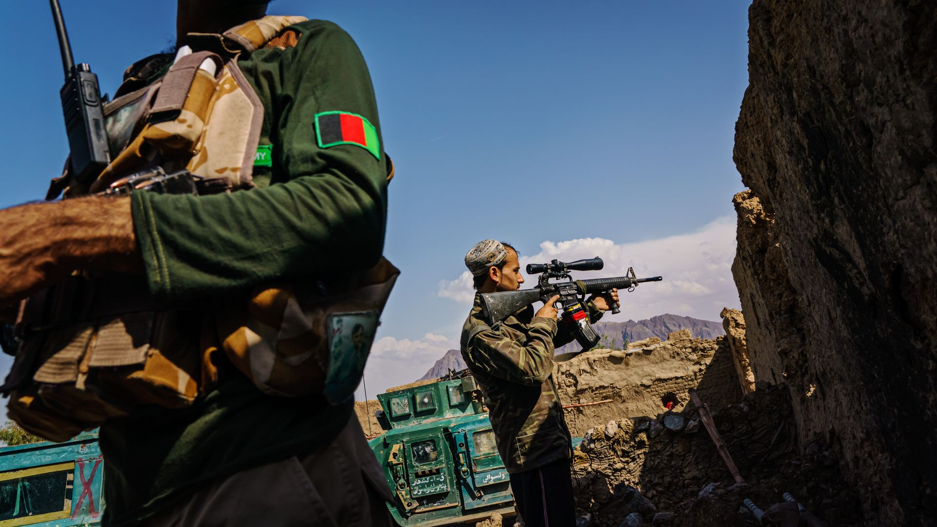 Photo of a soldier in an Afghan uniform in the foreground and another Afghan soldier aiming his rifle at an outpost