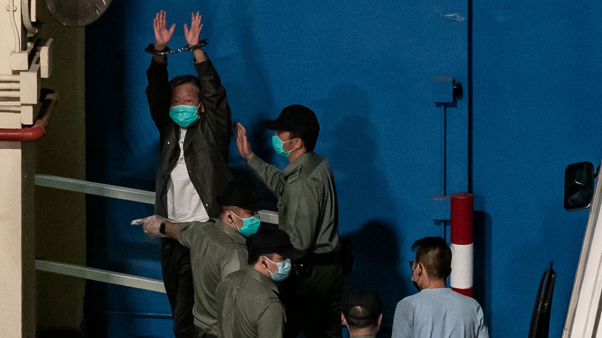 Photo of a person wearing handcuffs and raising their arms high while they are detained by police