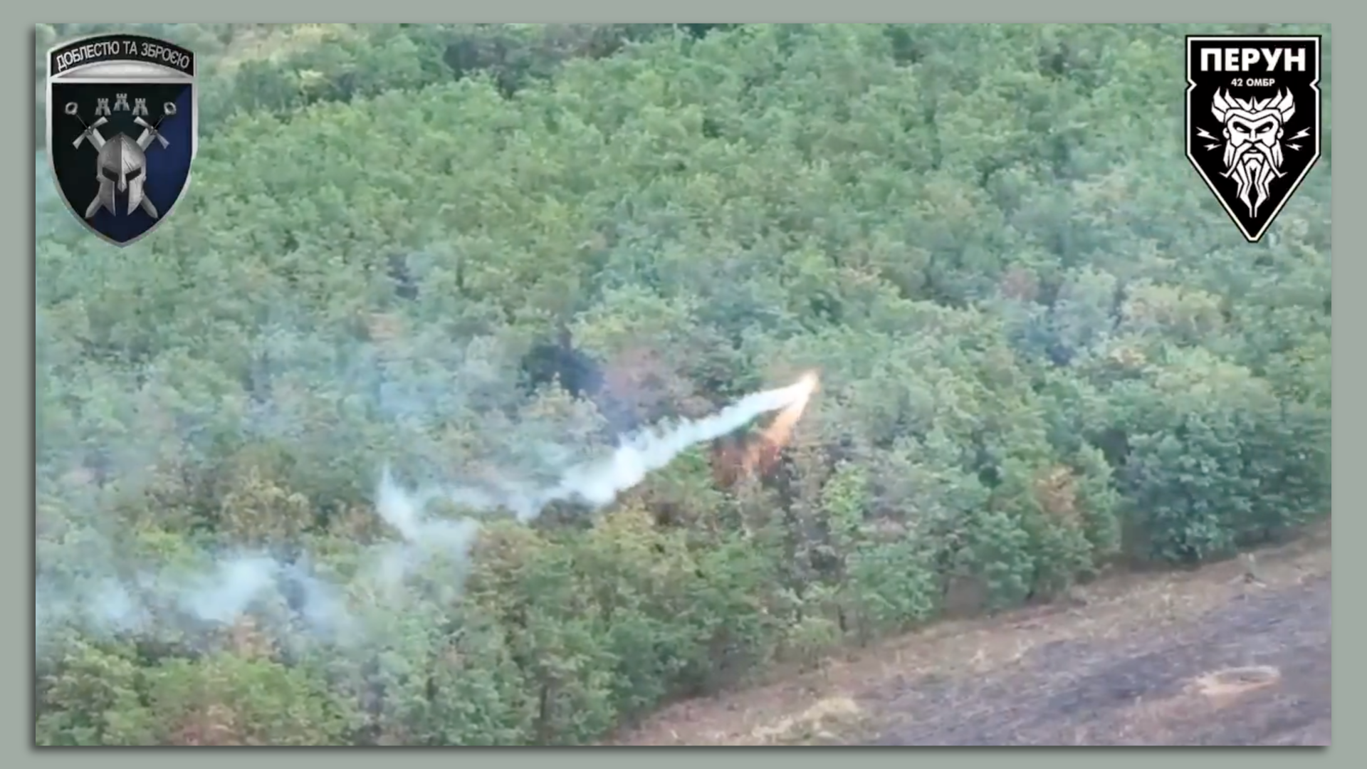 A Ukrainian drone drops what appears to be fire over a forest. Smoke is pouring out the back. Military logos adorn the corners of the screenshot.