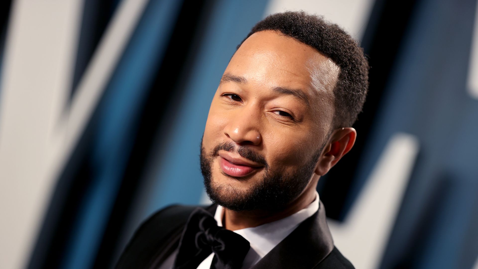 Singer John Legend stands on a red carpet in a tuxedo.