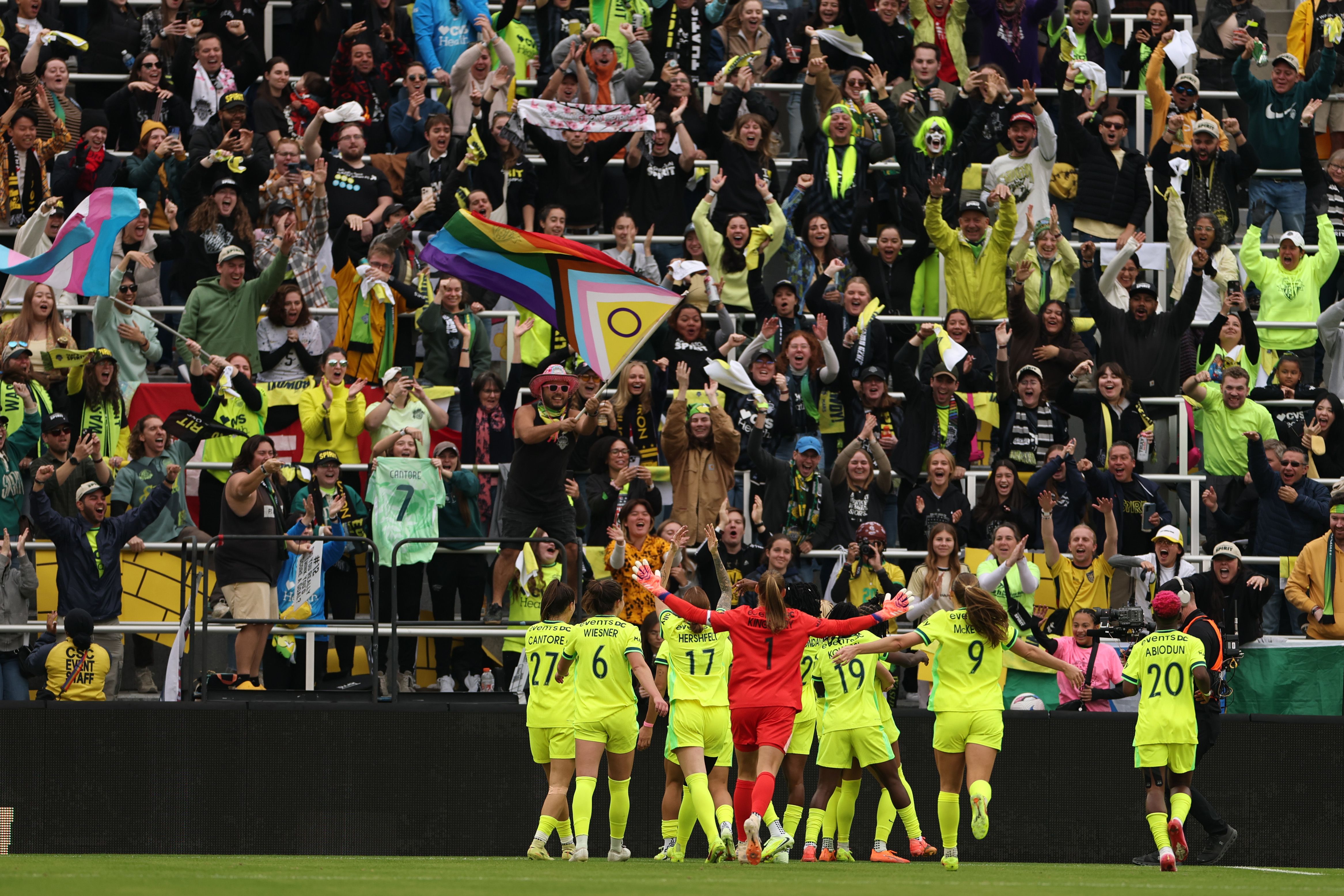 Spirits players in neon yellow jerseys cheer with the crowd