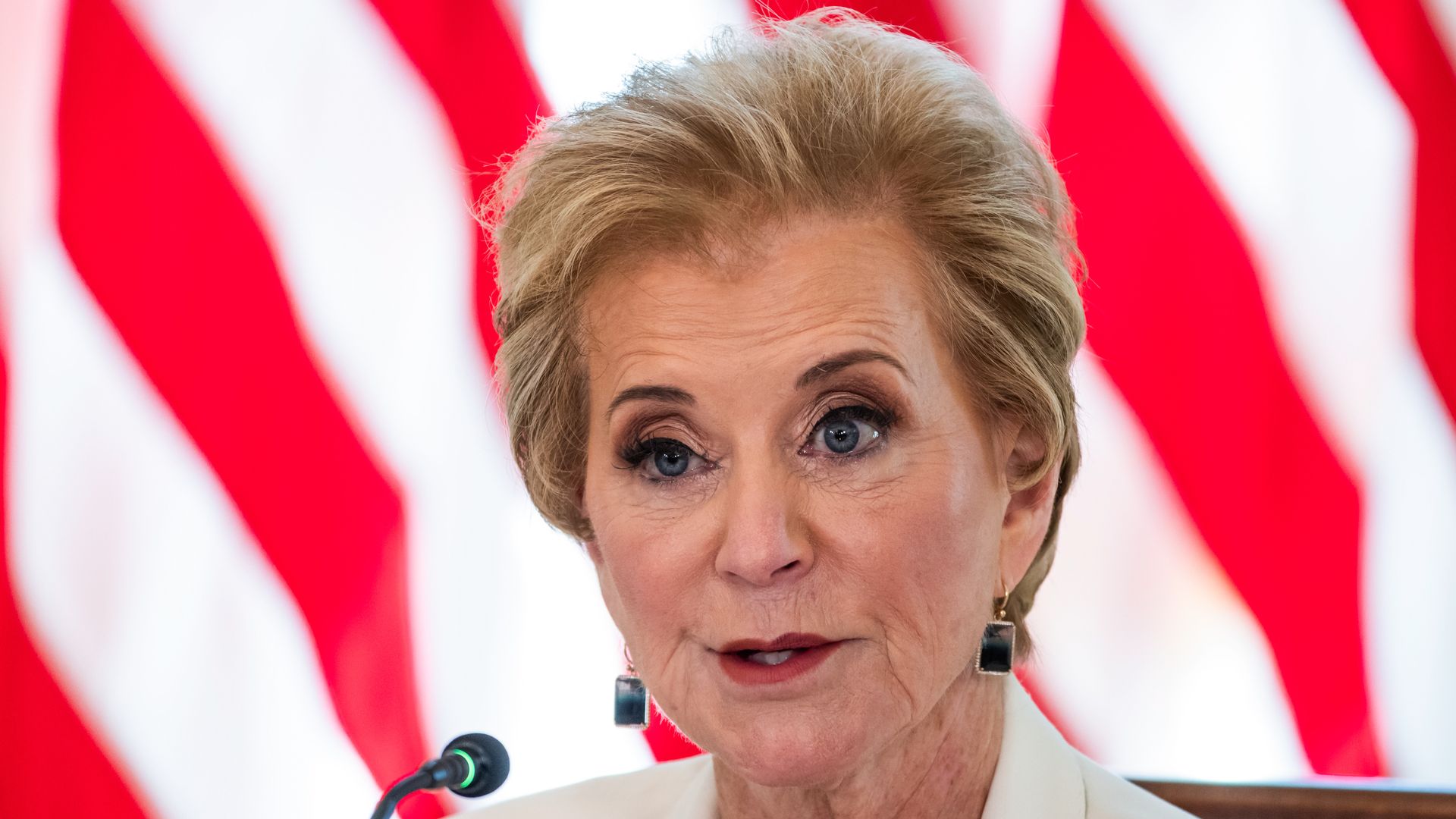 Linda McMahon, wearing a white top and square earrings, speaks into a microphone.