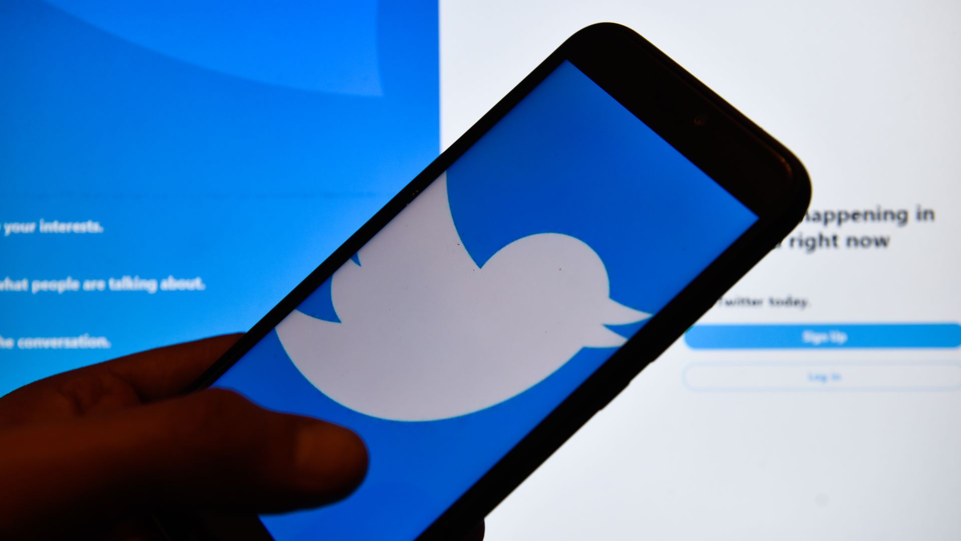 In this image, a person holds a phone with the Twitter logo on it.