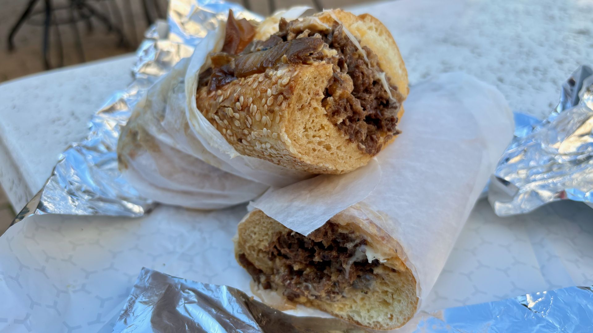 A close-up of two halves of a cheesesteak wrapped in parchment paper, on top of foil