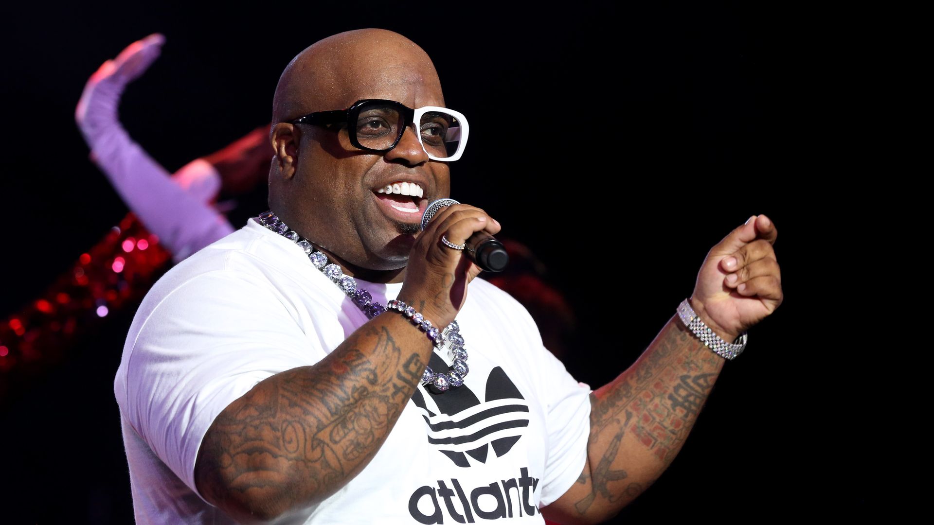 CeeLo Green sings while wearing a white Adidas t-shirt and glasses that are half white and half black. 