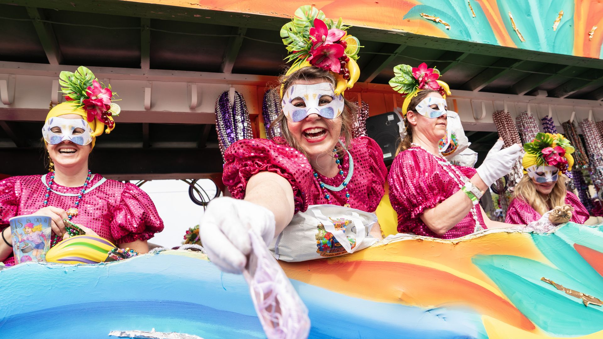 A float rider hands a pair of sunglasses down toward the camera.
