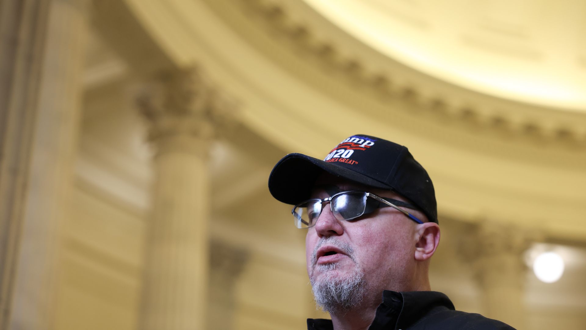 Stewart Rhodes, wearing a Trump 2020 hat, speaks to reporters (not pictured) from inside a Capitol Hill complex building.