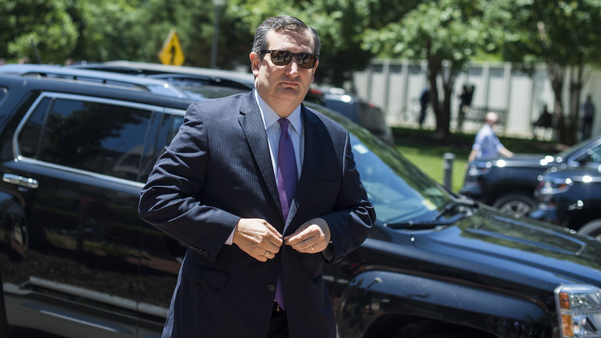Ted Cruz buttoning his blazer and wearing sun glasses