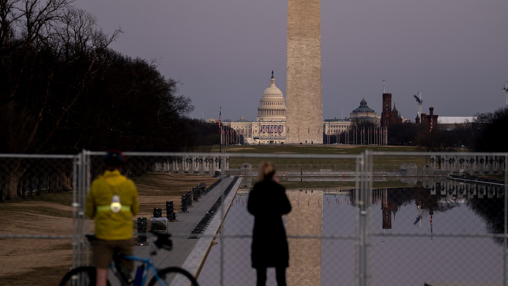 observers stand outside fencing surrounding the reflecting pool
