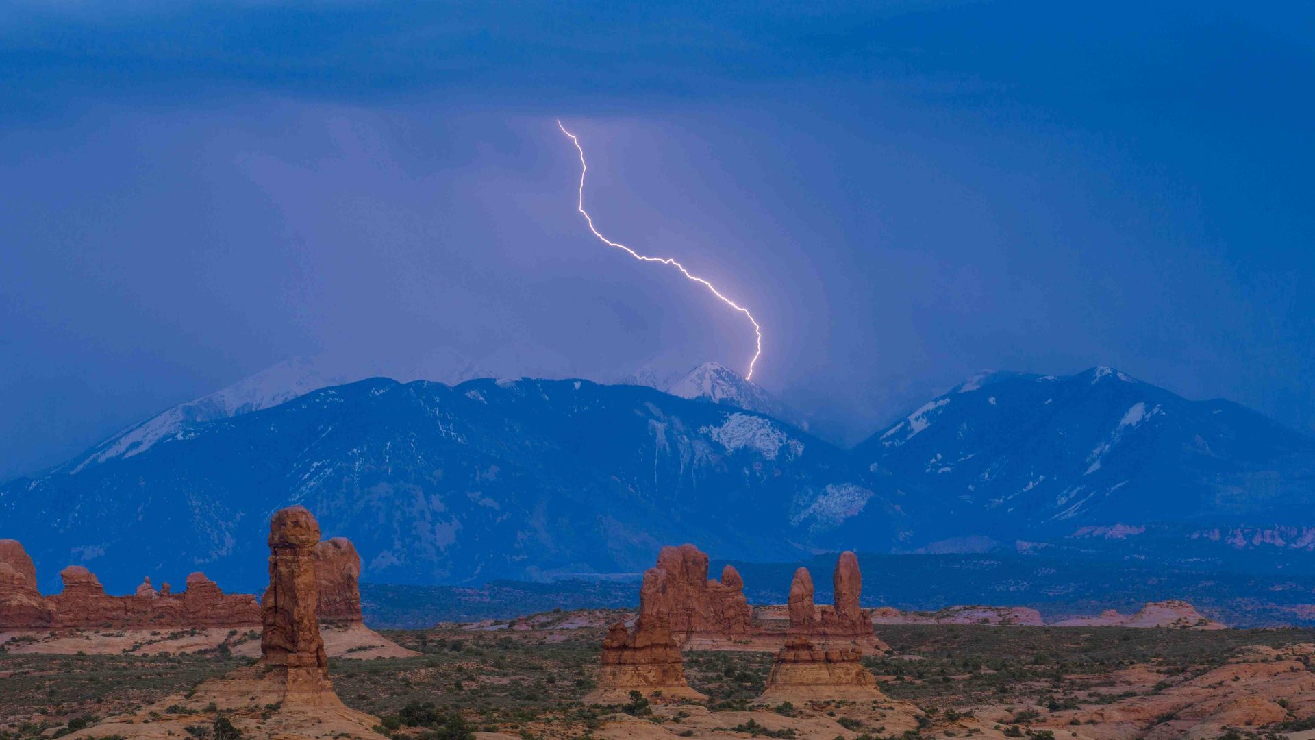 Lightning hits a mountain range behind red rock formations