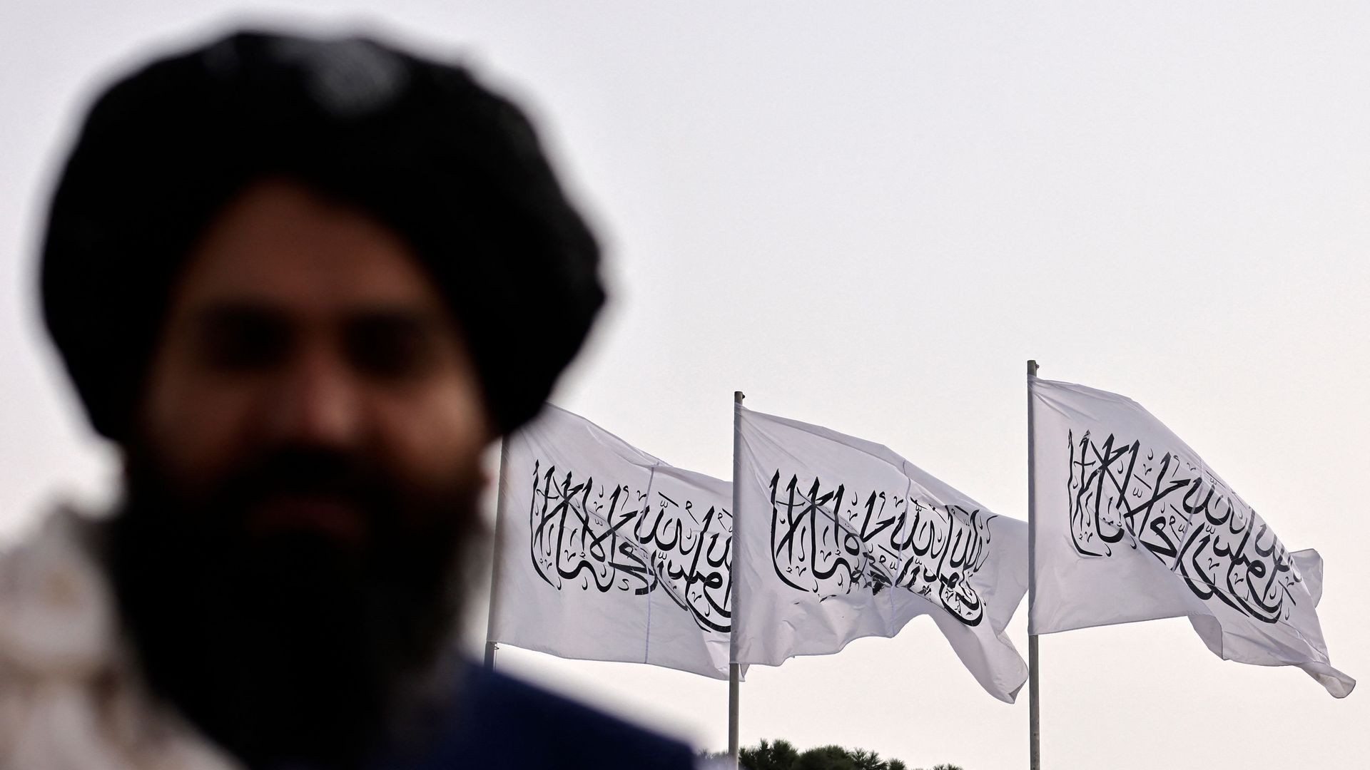 Photo of a man in front of the Taliban flag.