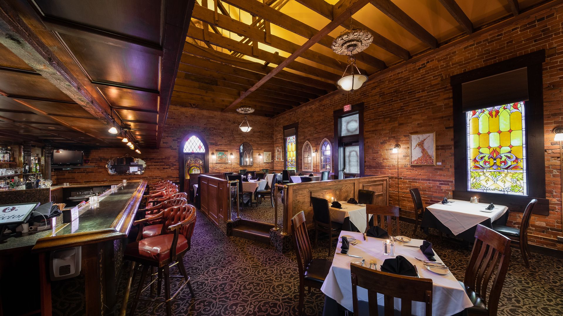 The interior of the Refectory, with a bar, exposed wood ceiling beams and stained glass windows